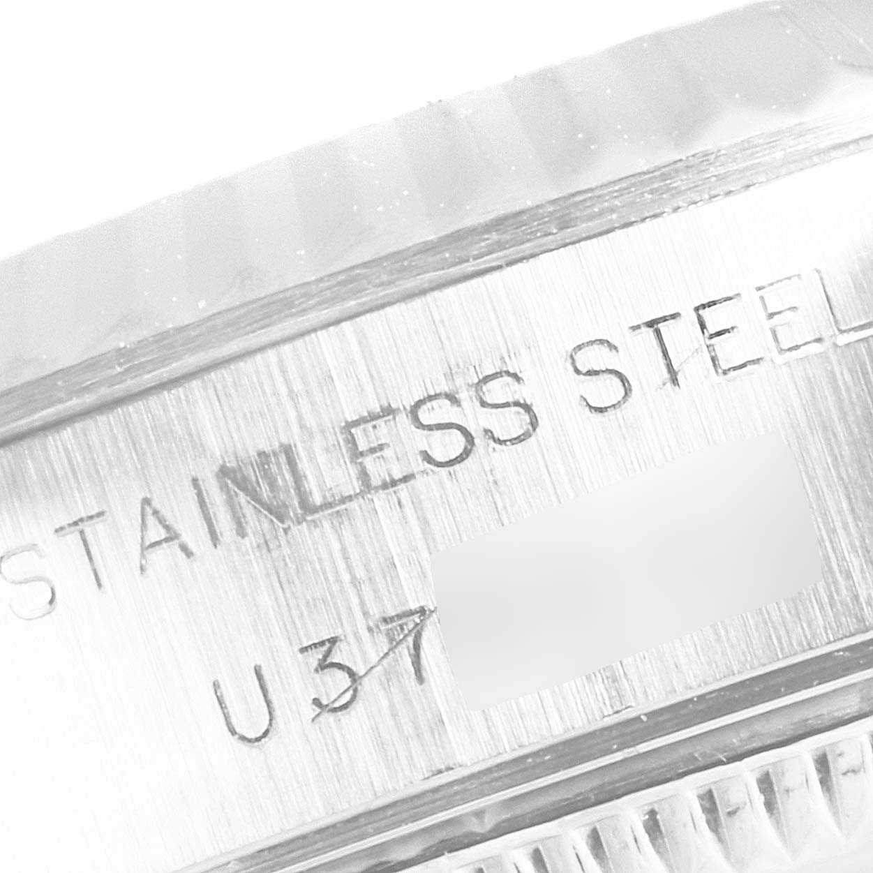 The image shows a close-up of the side edge of a Rolex Datejust 69174 Women's Stainless Steel Blue Dial 69174 Women's Stainless Steel Blue Dial watch featuring its stainless steel inscription and a partial serial number.