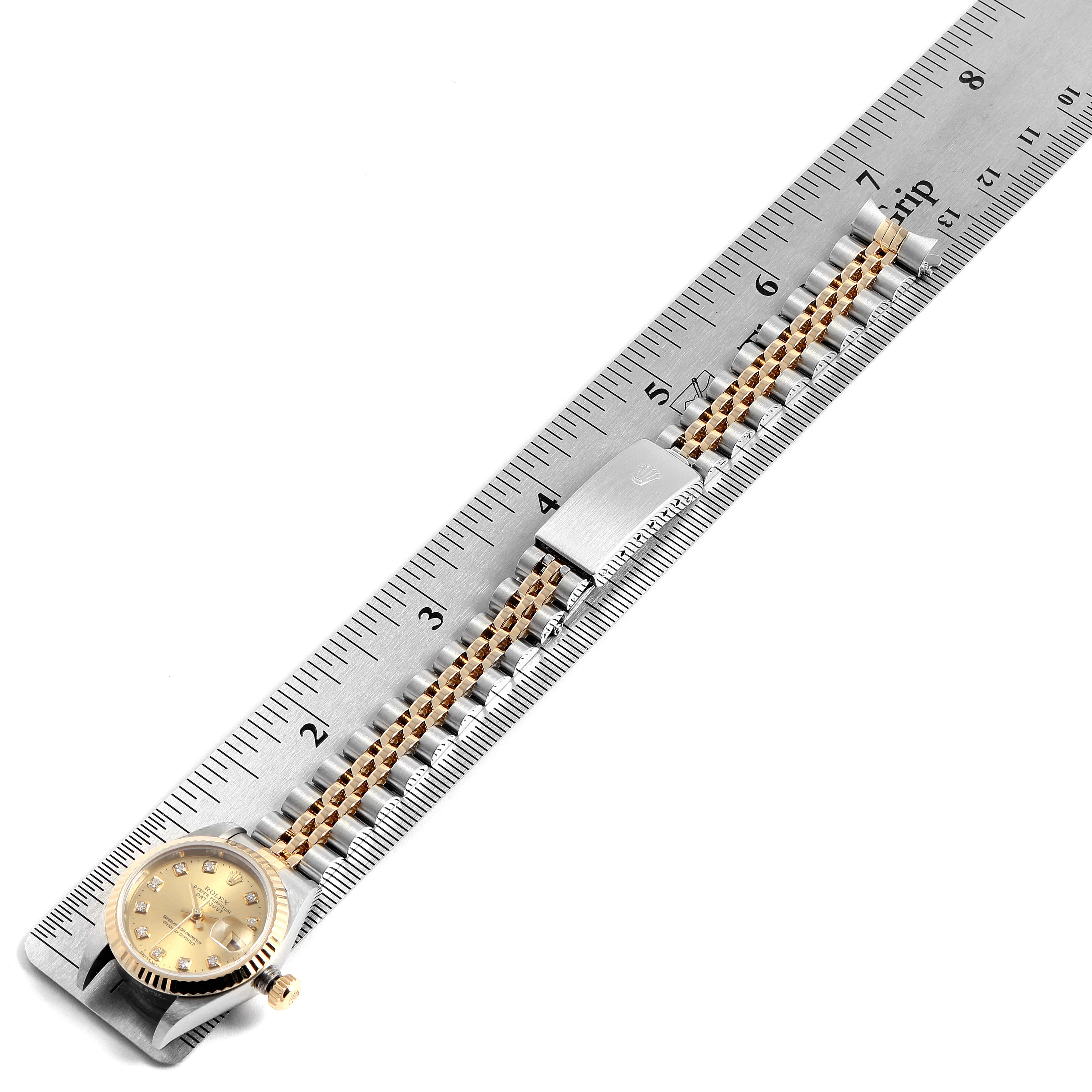 This image shows a Rolex Datejust 79173 Women's Steel and Gold (two tone) Champagne Dial 79173 Women's Steel and Gold (two tone) Champagne Dial watch laid diagonally on a metal ruler, highlighting the gold and silver strap and the clasp.