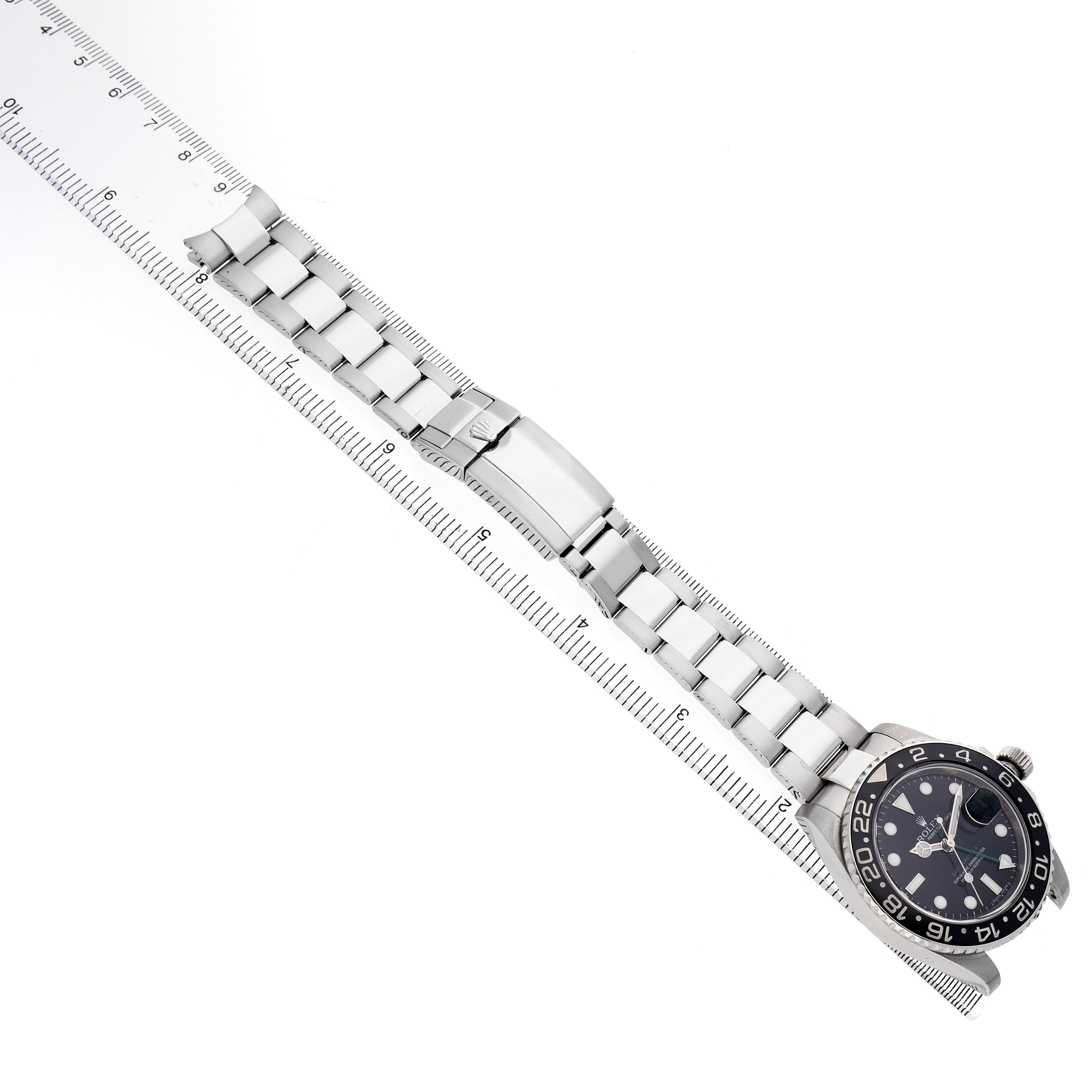 The Rolex GMT-Master 116710 Men's Stainless Steel Black Dial watch is shown from a top-down angle, including the watch face, bezel, bracelet, and clasp, alongside a ruler.