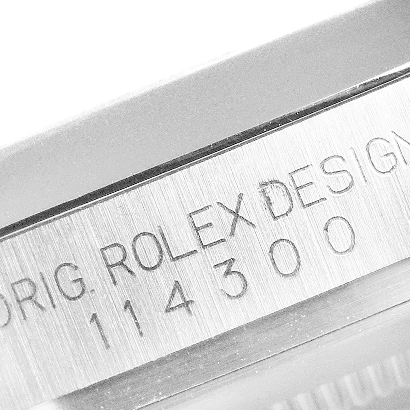 The image shows a close-up of the side of a Rolex Oyster Perpetual 114300 Men's Stainless Steel Silver Dial 114300 Men's Stainless Steel Silver Dial watch, focusing on the case engraving.
