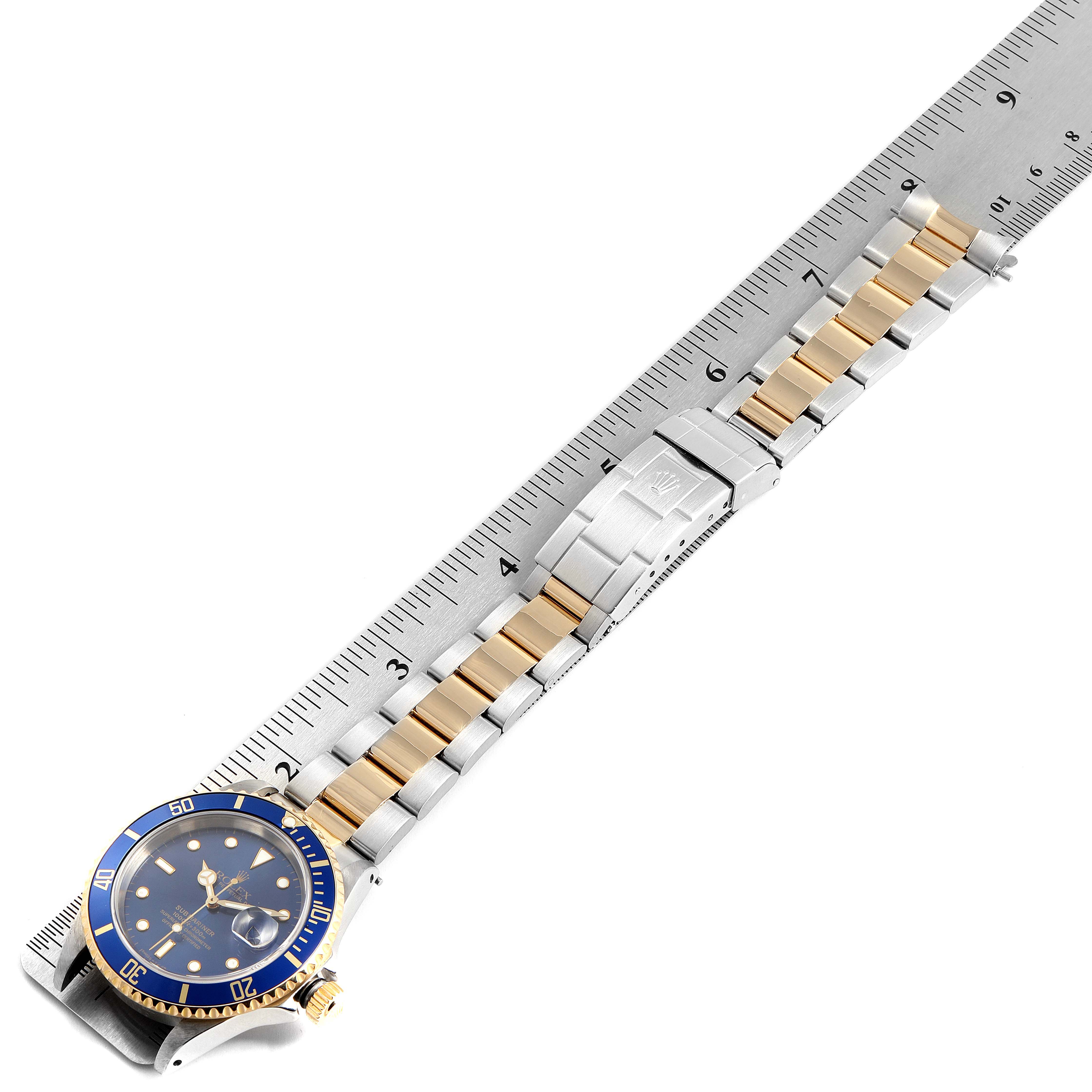 The image shows a Rolex Submariner 16613 Men
s Stainless Steel Blue Dial 16613 Men
s Stainless Steel Blue Dial watch with a blue bezel and a two-tone metal bracelet, measured against a ruler.