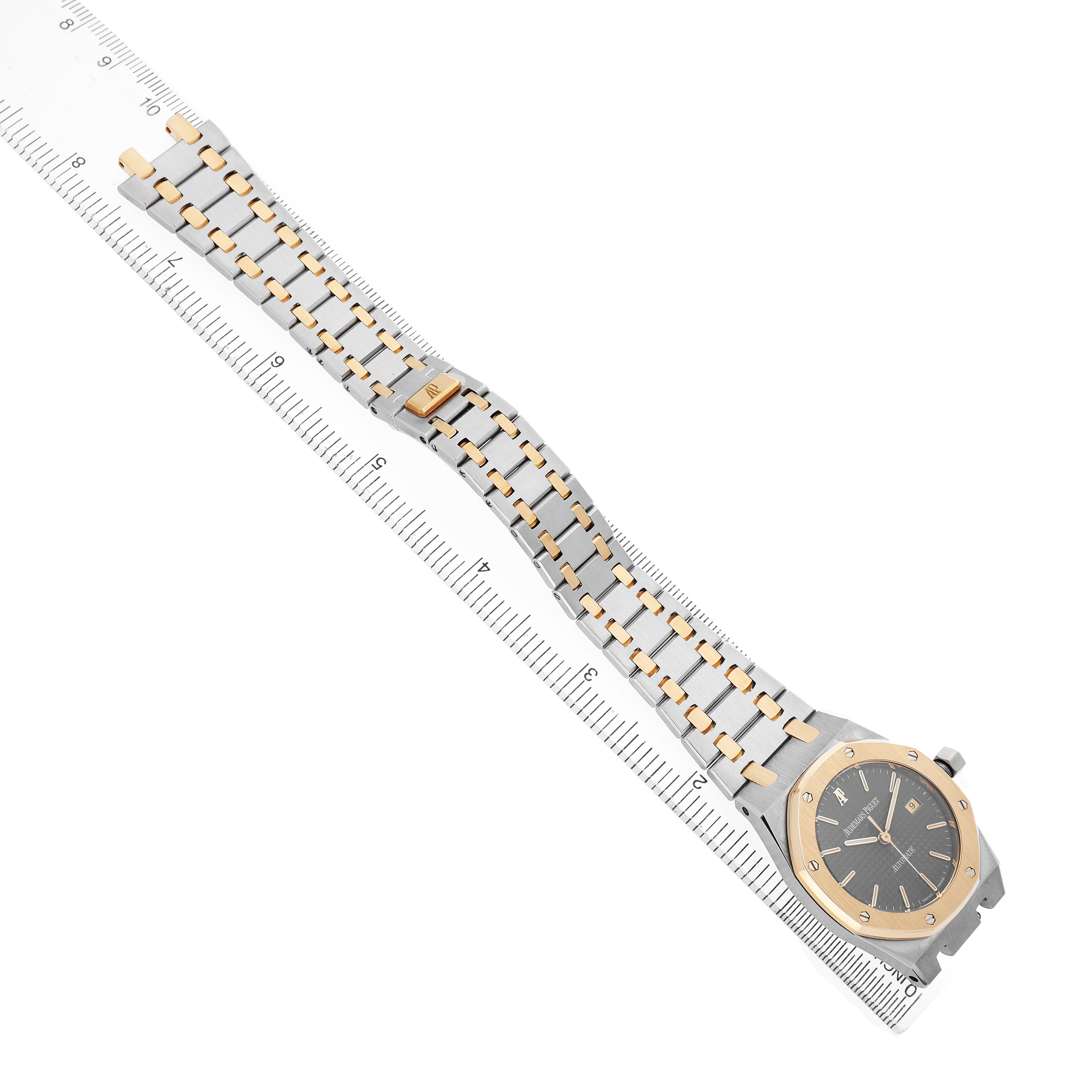 The Audemars Piguet Royal Oak 14100SA Men's Steel and Gold (two tone) Grey Dial watch is shown at an oblique angle, highlighting its face, bracelet, and clasp along a ruler.