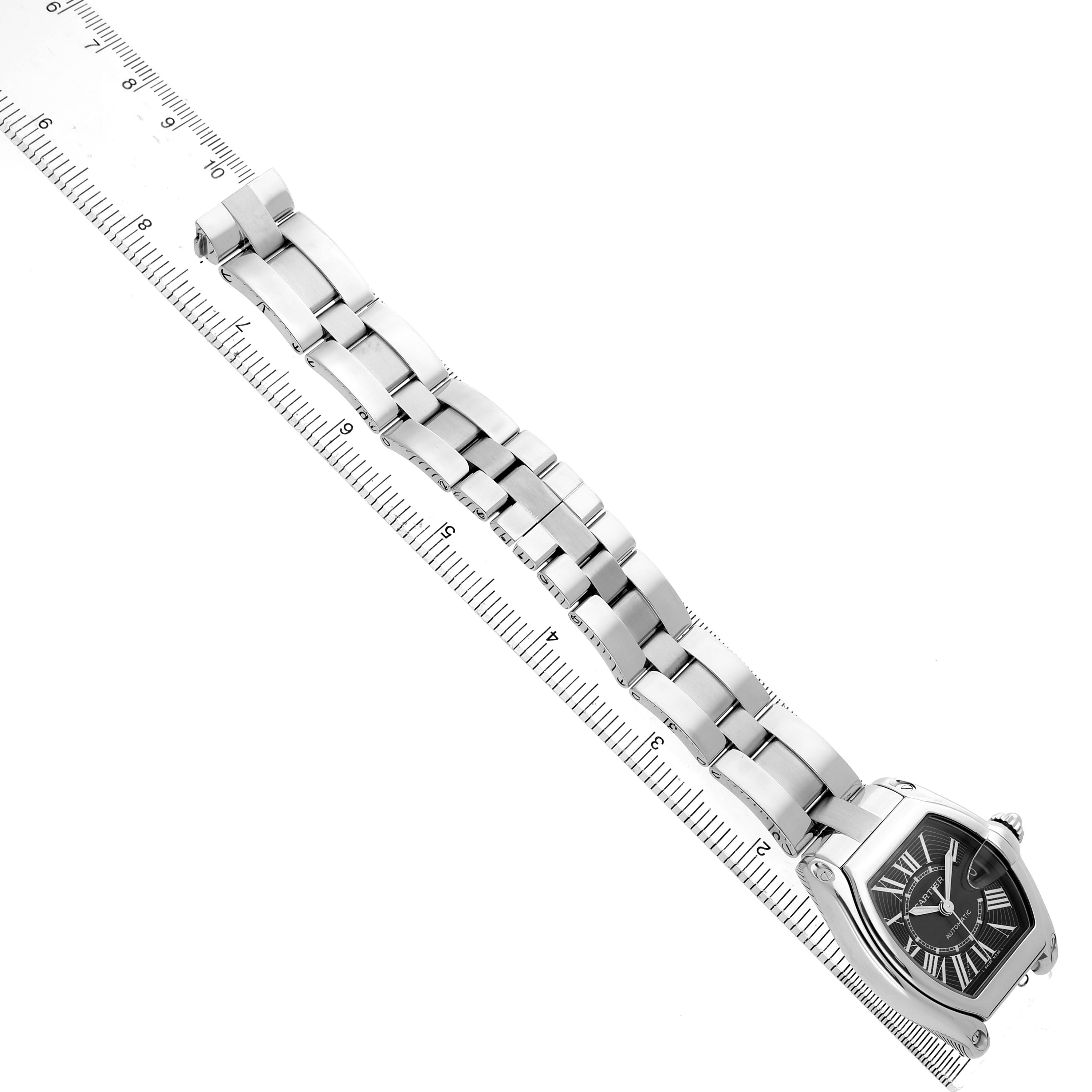 The image shows the Cartier Roadster W62041V3 Men's Stainless Steel Black Dial watch at a diagonal angle, highlighting its face and metal bracelet alongside a ruler.