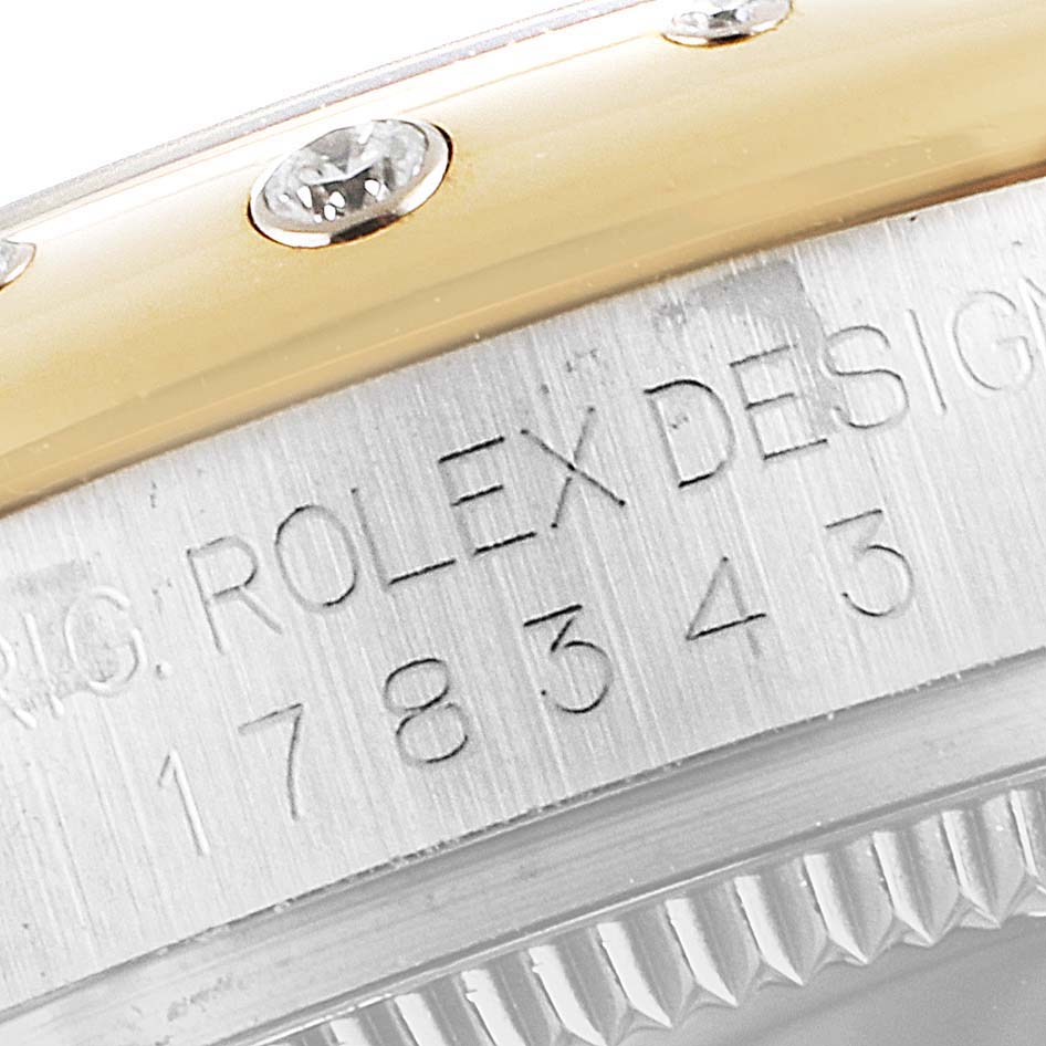 The image shows a close-up of the bezel and side of the case of a Mid-Size Rolex watch, featuring diamonds and engraved numbers.