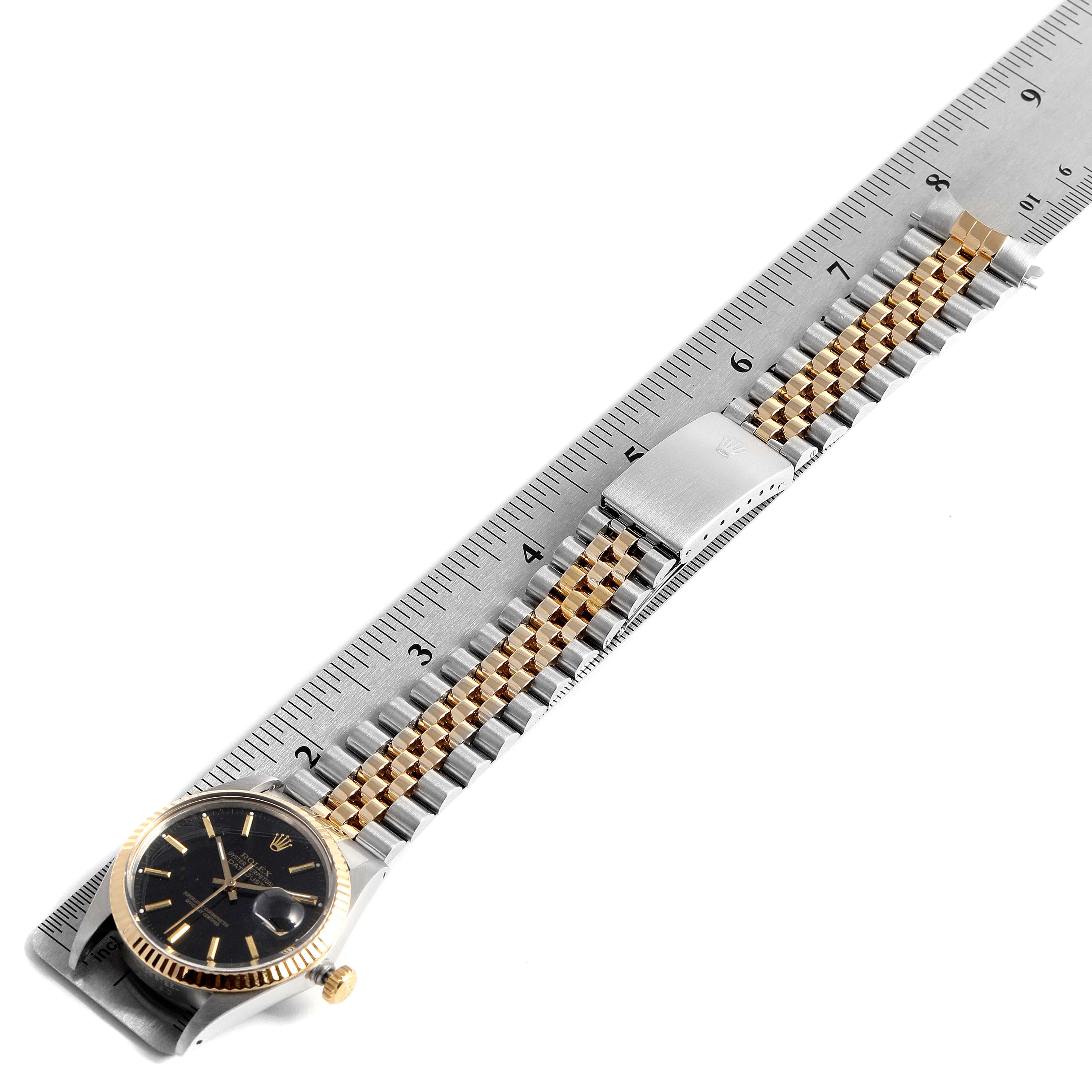 The Rolex Datejust 16013 Men's Steel and Gold (two tone) Black Dial 16013 Men's Steel and Gold (two tone) Black Dial watch is shown from an oblique angle, revealing the watch face, bracelet, clasp, and a portion of a ruler.