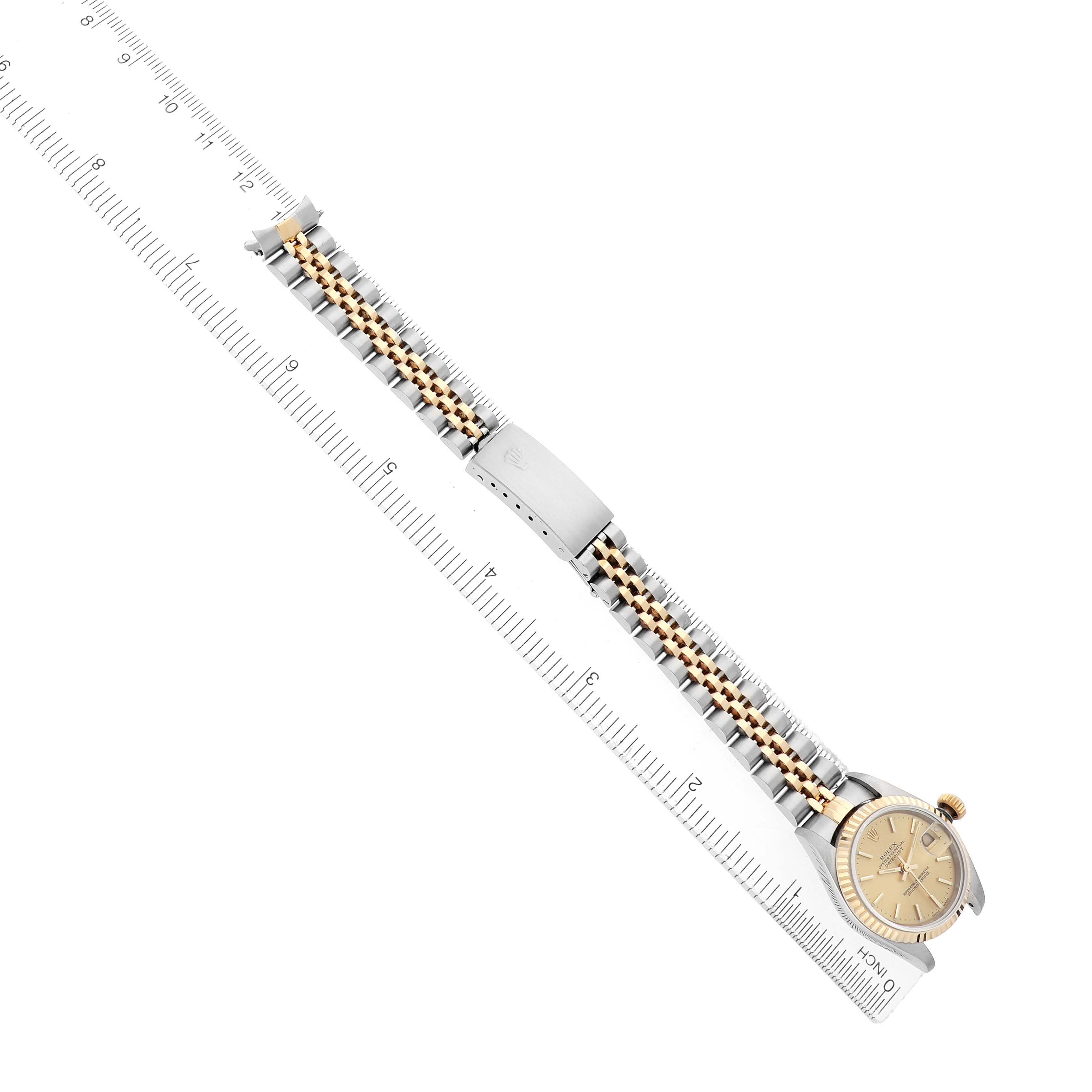 The image shows a Rolex Datejust 79173 Women
s Steel and Gold (two tone) Champagne Dial watch viewed from above, showcasing its face, bracelet, and clasp alongside a ruler for scale.
