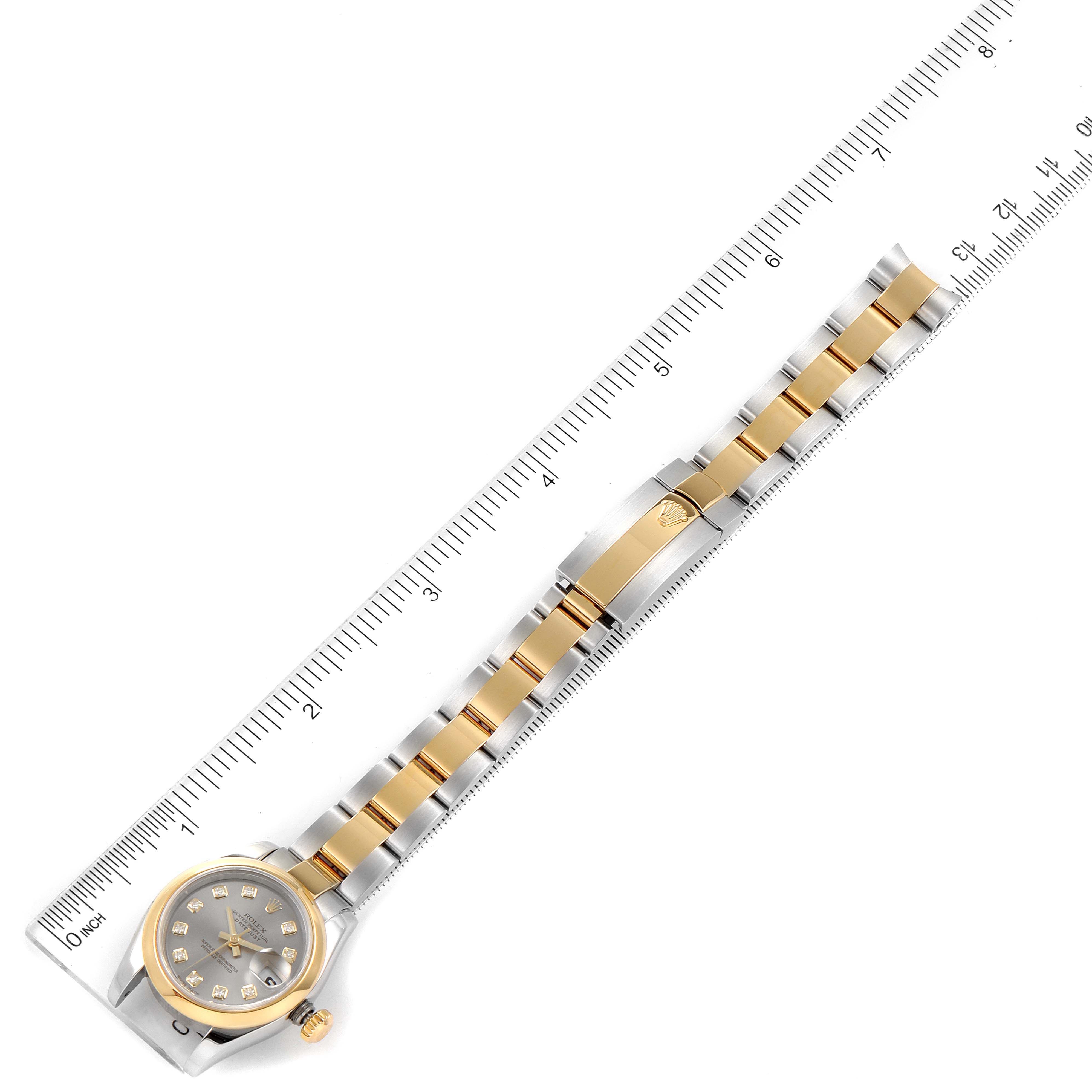 This image showcases the entire Rolex Datejust 179163 Women
s Steel and Gold (two tone) Grey Dial 179163 Women
s Steel and Gold (two tone) Grey Dial watch from an aerial view, including the face, bezel, and two-tone bracelet alongside a ruler.