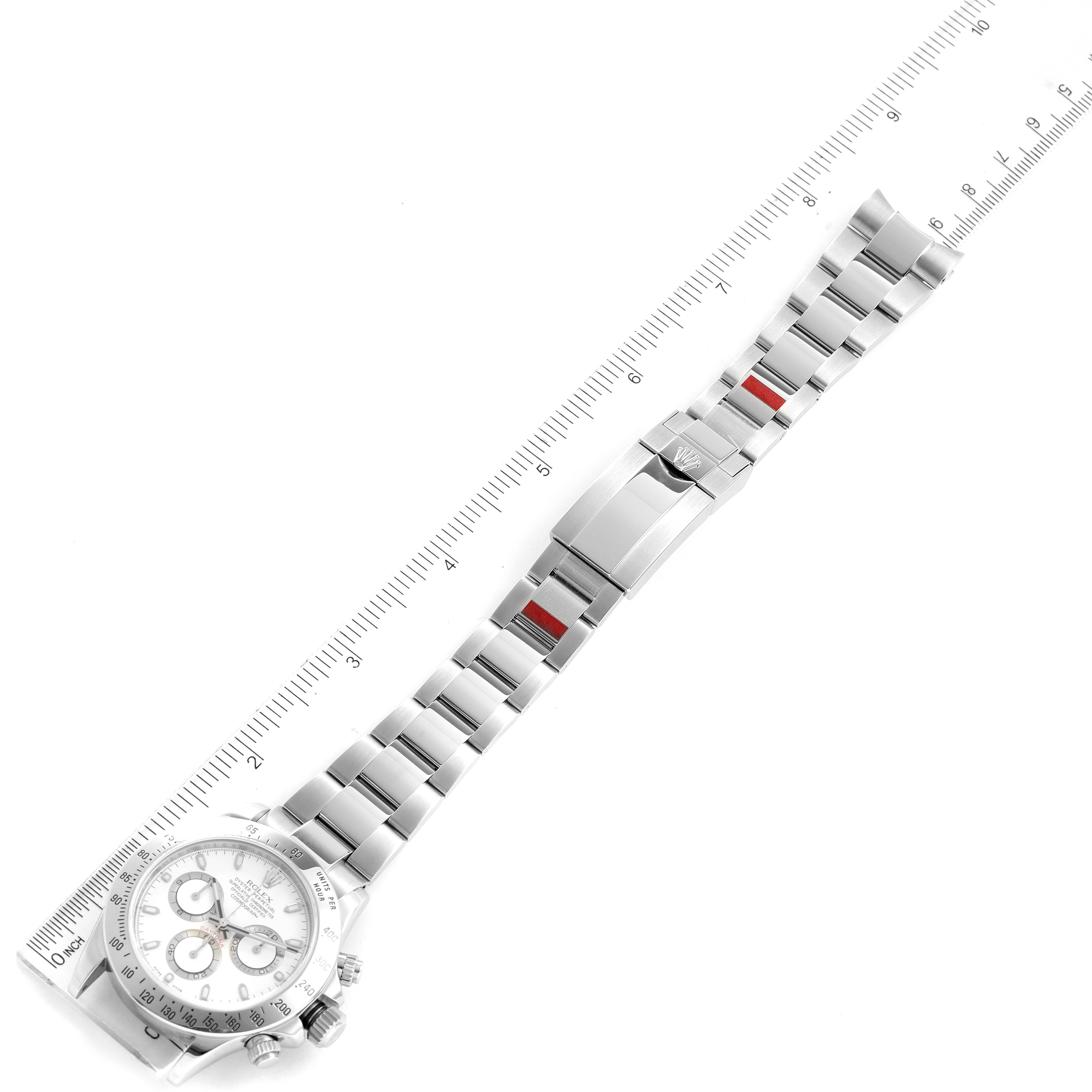 This image shows a Rolex Daytona 116520 Men's Stainless Steel White Dial 116520 Men's Stainless Steel White Dial watch lying flat with its bracelet and clasp extended, alongside a ruler for scale.