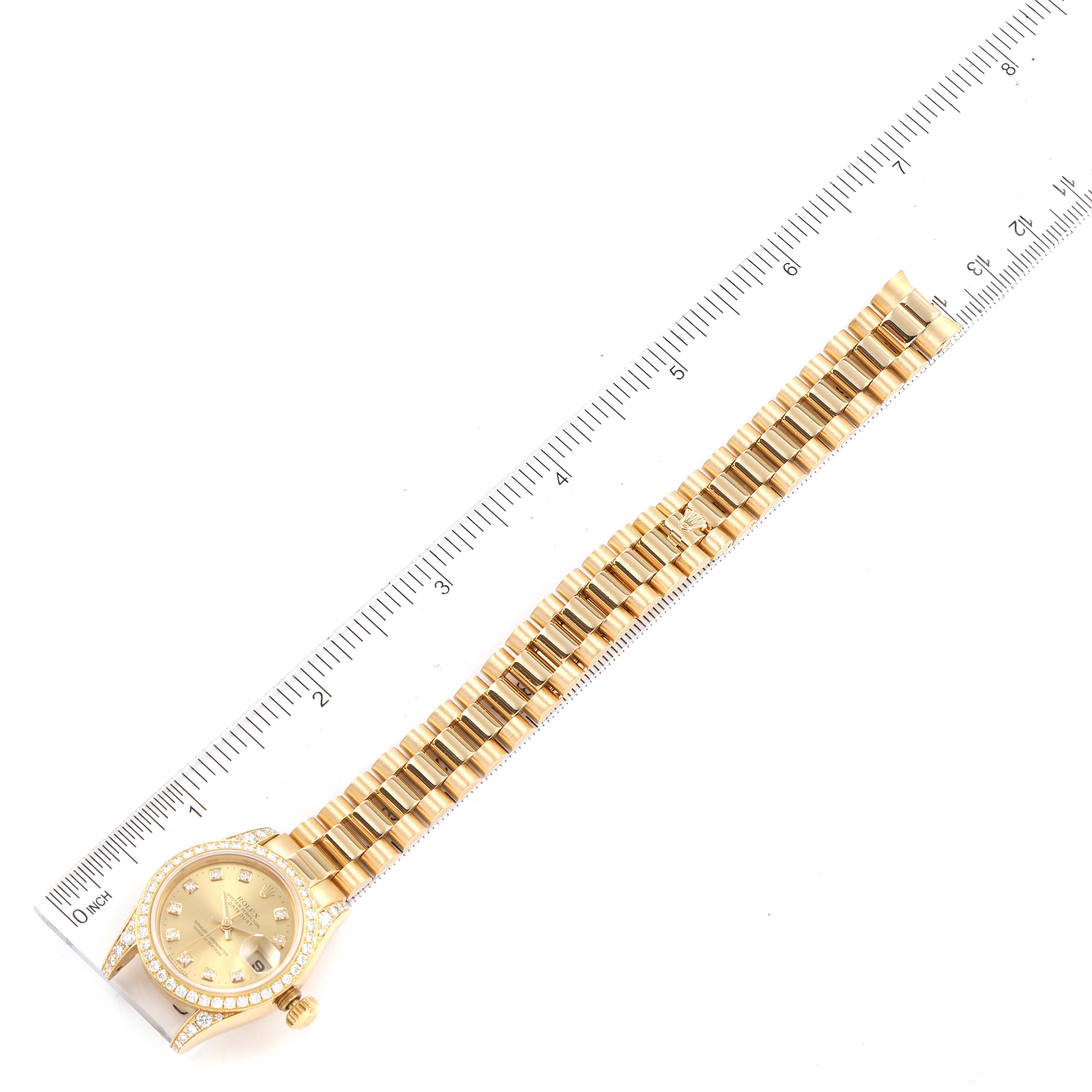 The image shows a top-down view of a Rolex President 179158 Women's Yellow Gold Champagne Dial 179158 Women's Yellow Gold Champagne Dial model watch, including its face, crown, and entire bracelet, alongside a ruler.
