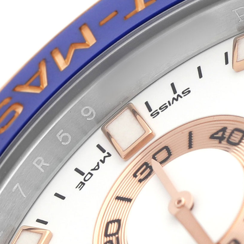 The image shows a close-up of the Rolex Yacht-Master 116681 Men's Steel and Gold (two tone) White Dial's bezel, dial, and part of the hand, featuring blue and gold accents.
