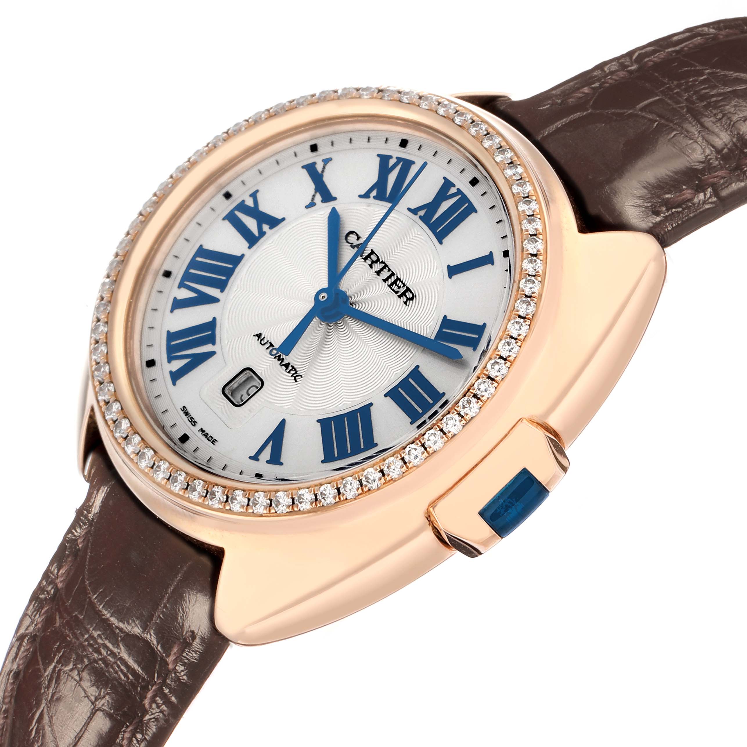 The Cartier Clé watch is shown at a slight angle, highlighting its round face, sapphire-set crown, and leather strap.