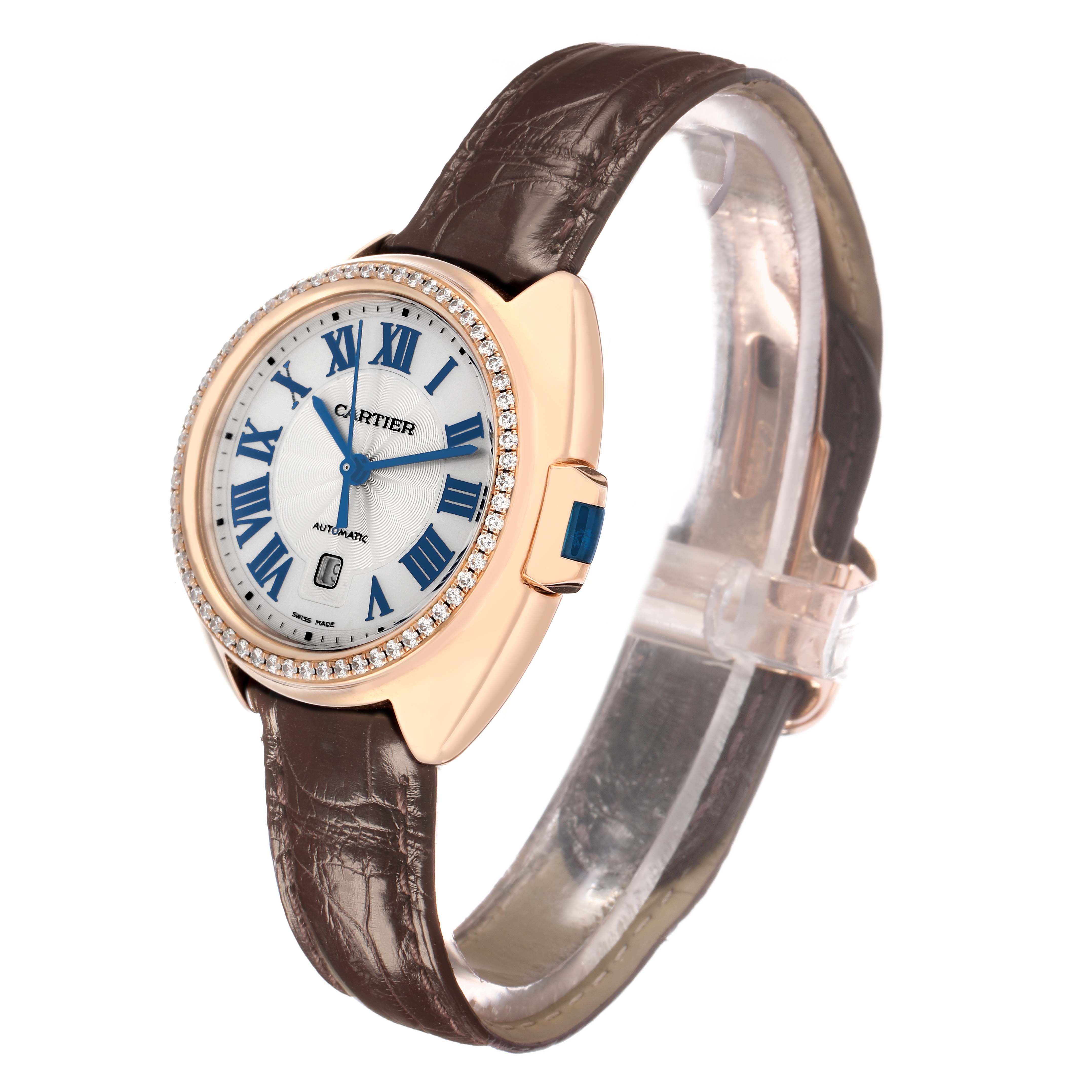 The Cartier Clé watch is shown at a three-quarter angle, displaying its face, leather strap, and diamond-encrusted bezel.