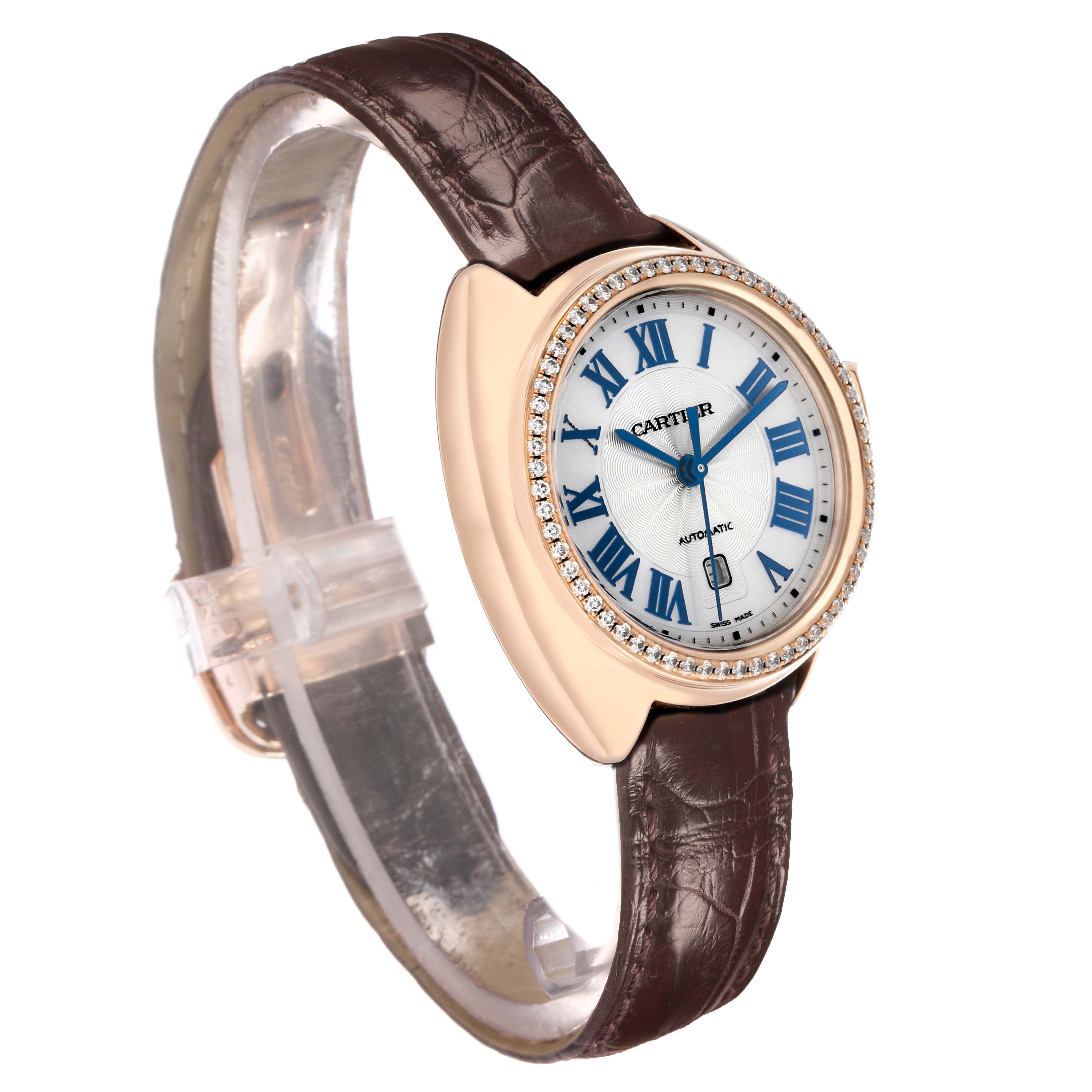 The Cartier Clé watch is shown at a three-quarter angle, featuring a brown leather strap and diamond-encrusted bezel.
