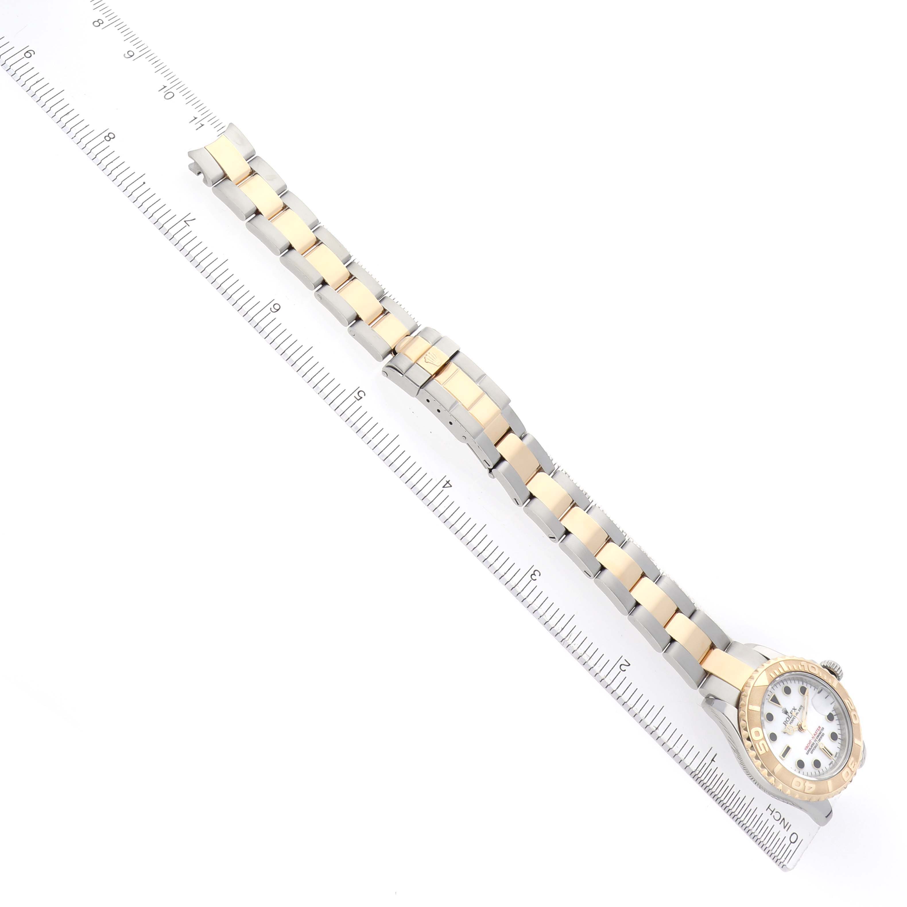 The Rolex Yacht-Master 169623 Women's Steel and Gold (two tone) White Dial watch is laid flat, showing the full length of the band and part of the watch face with a ruler alongside.