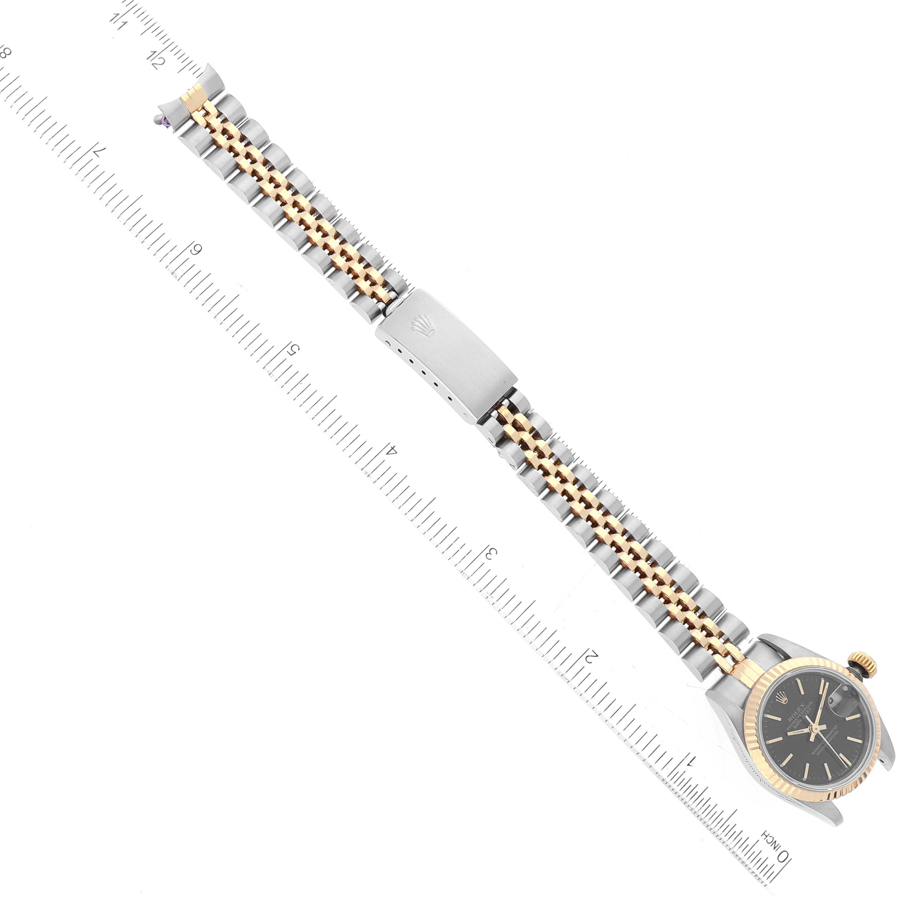 The image shows a top view of a Rolex Datejust 69173 Women's Steel and Gold (two tone) Black Dial 69173 Women's Steel and Gold (two tone) Black Dial watch, highlighting the watch face, bracelet, and clasp against a background with a ruler.
