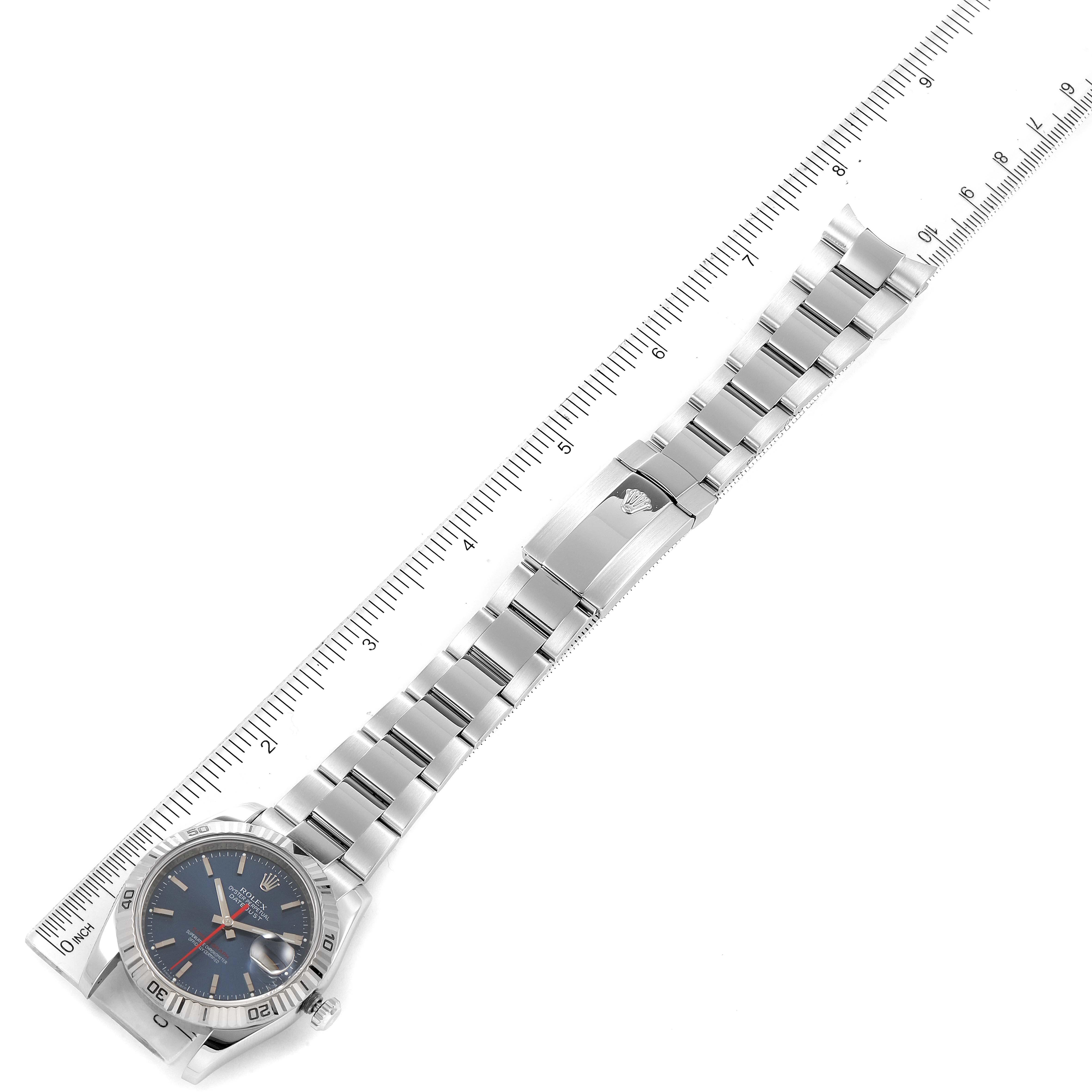 The Rolex Turn-o-Graph 116264 Men's Stainless Steel Blue Dial 116264 Men's Stainless Steel Blue Dial watch is shown in a flat lay view alongside a ruler, displaying its entire bracelet and face.