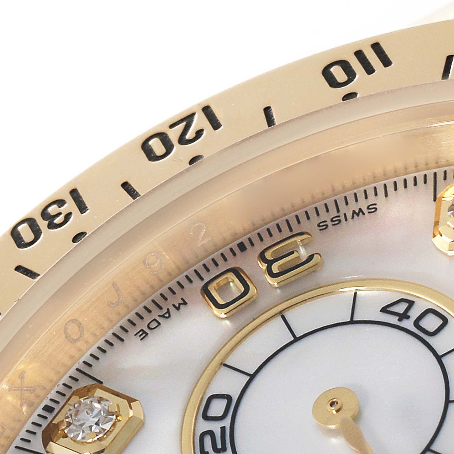 This image shows a close-up of the Rolex Daytona 116528 Men's Yellow Gold Mother of Pearl Dial 116528 Men's Yellow Gold Mother of Pearl Dial watch's bezel, dial, diamond marker, and part of the chronograph.
