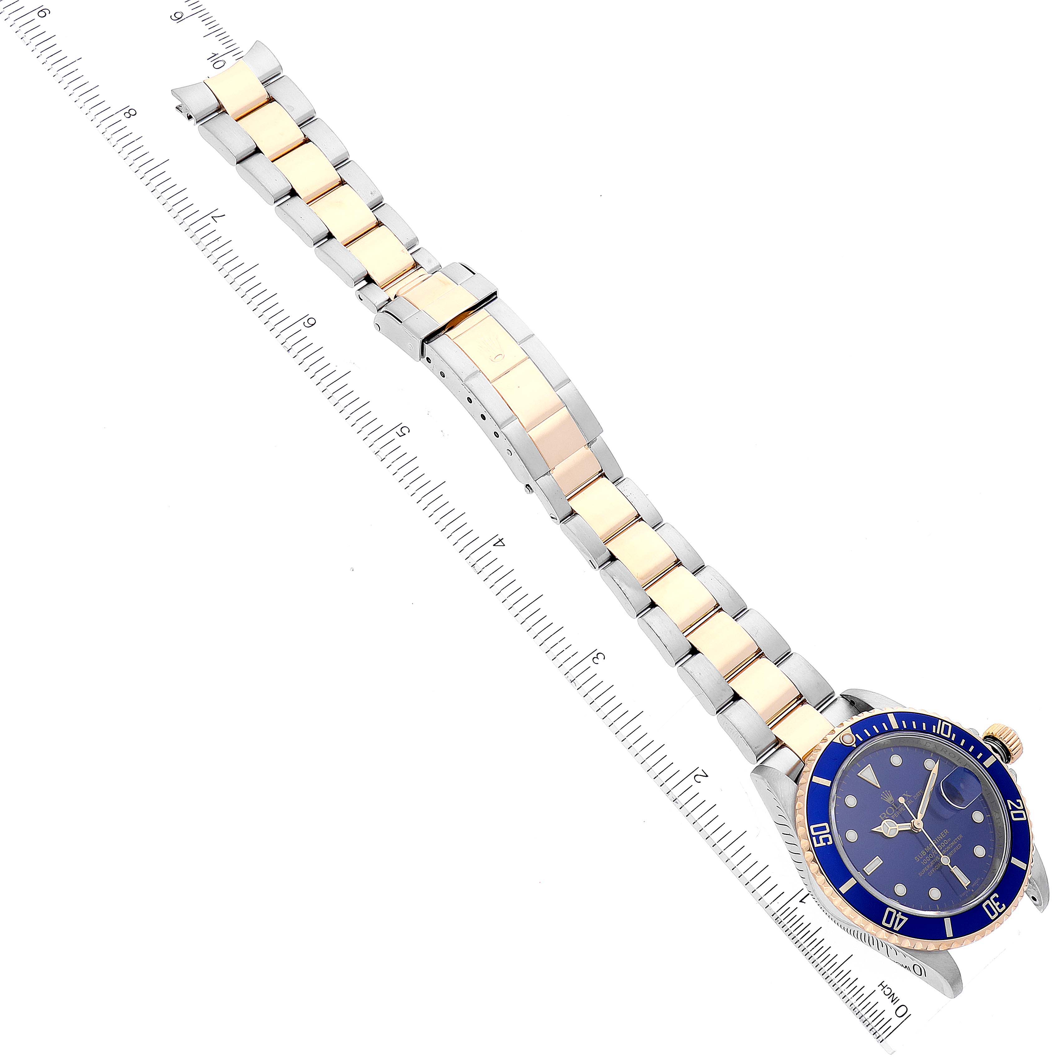 The image shows a top-down view of a Rolex Submariner 16613 Men's Steel and Gold (two tone) Blue Dial 16613 Men's Steel and Gold (two tone) Blue Dial watch with its full gold and silver bracelet, alongside a ruler for scale.
