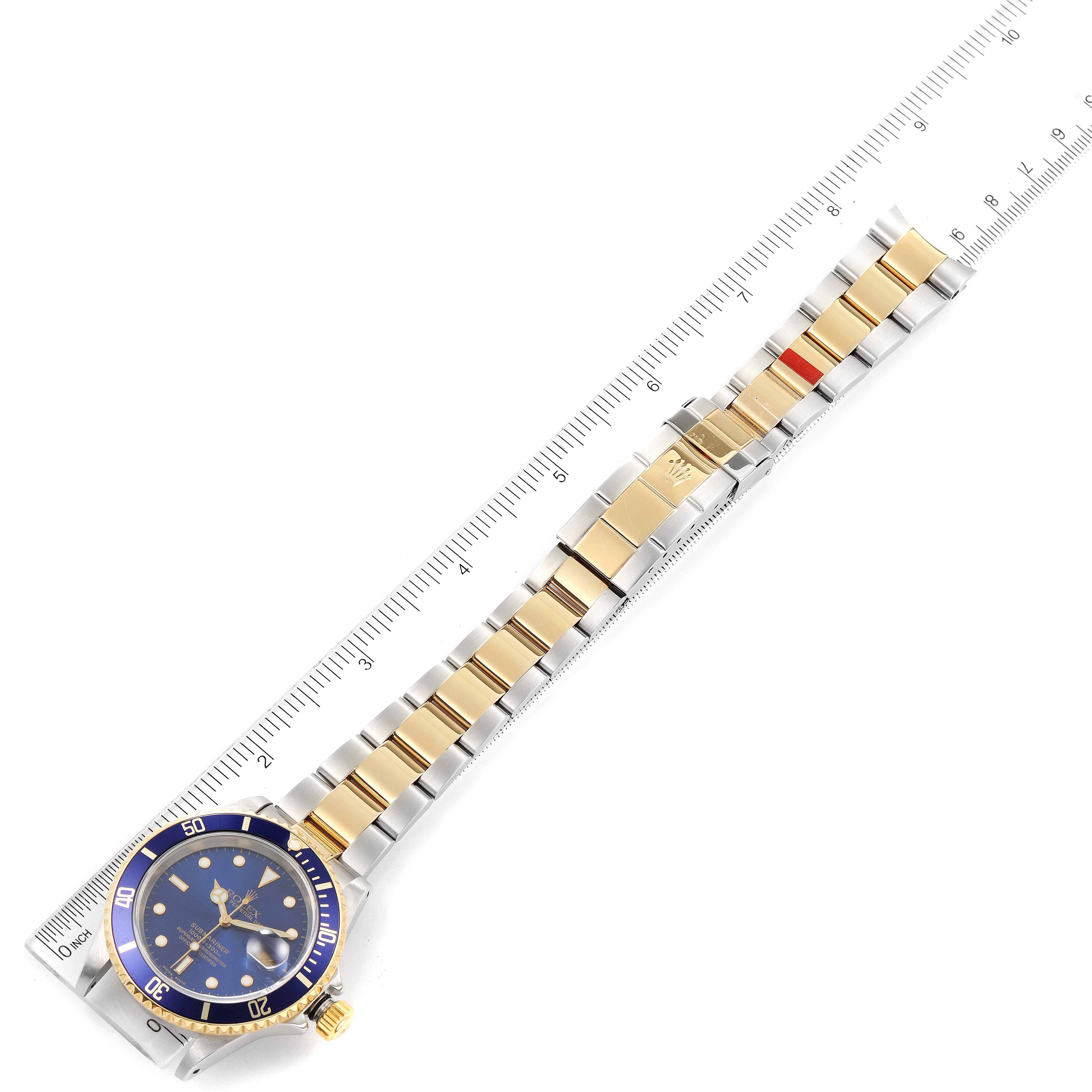 The image shows a top-down view of a Rolex Submariner 16613 Men's Steel and Gold (two tone) Blue Dial 16613 Men's Steel and Gold (two tone) Blue Dial watch, featuring the face, bezel, and bracelet laid next to a ruler.