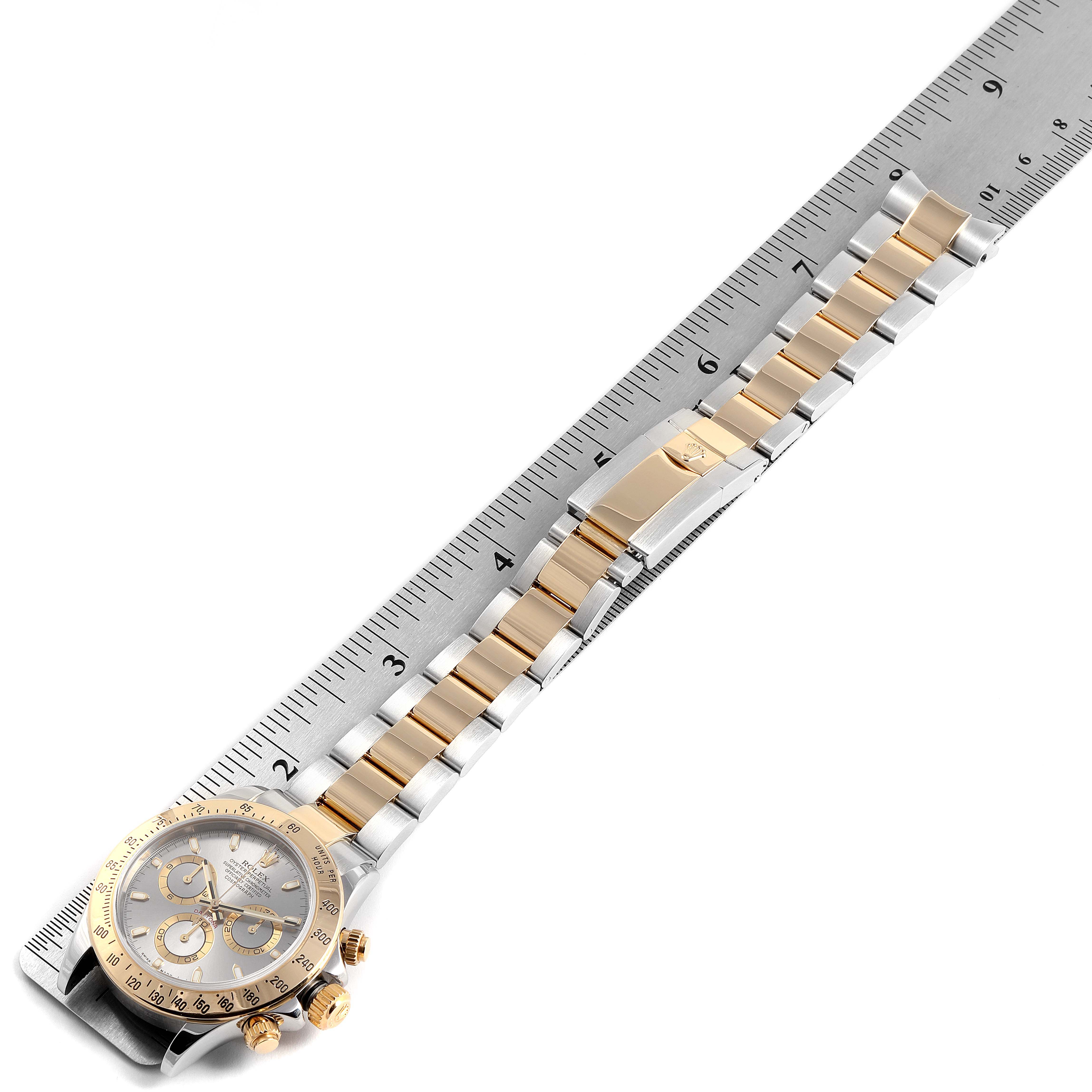 The image shows a side view of a Rolex Daytona 16523 Men's Steel and Gold (two tone) Grey Dial 16523 Men's Steel and Gold (two tone) Grey Dial watch, including its face, bezel, bracelet, and clasp, being measured with a ruler.