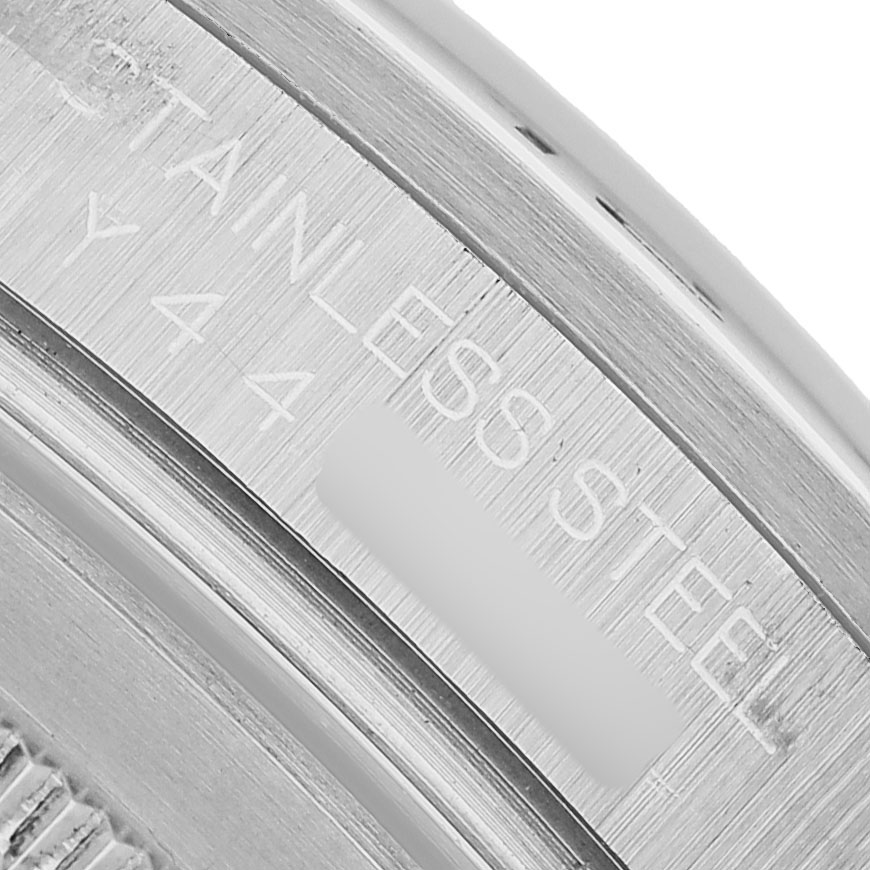 The image shows a close-up of the engraving on the inner bezel of a Rolex Explorer 16570 Men's Stainless Steel White Dial, highlighting "STAINLESS STEEL" wording.