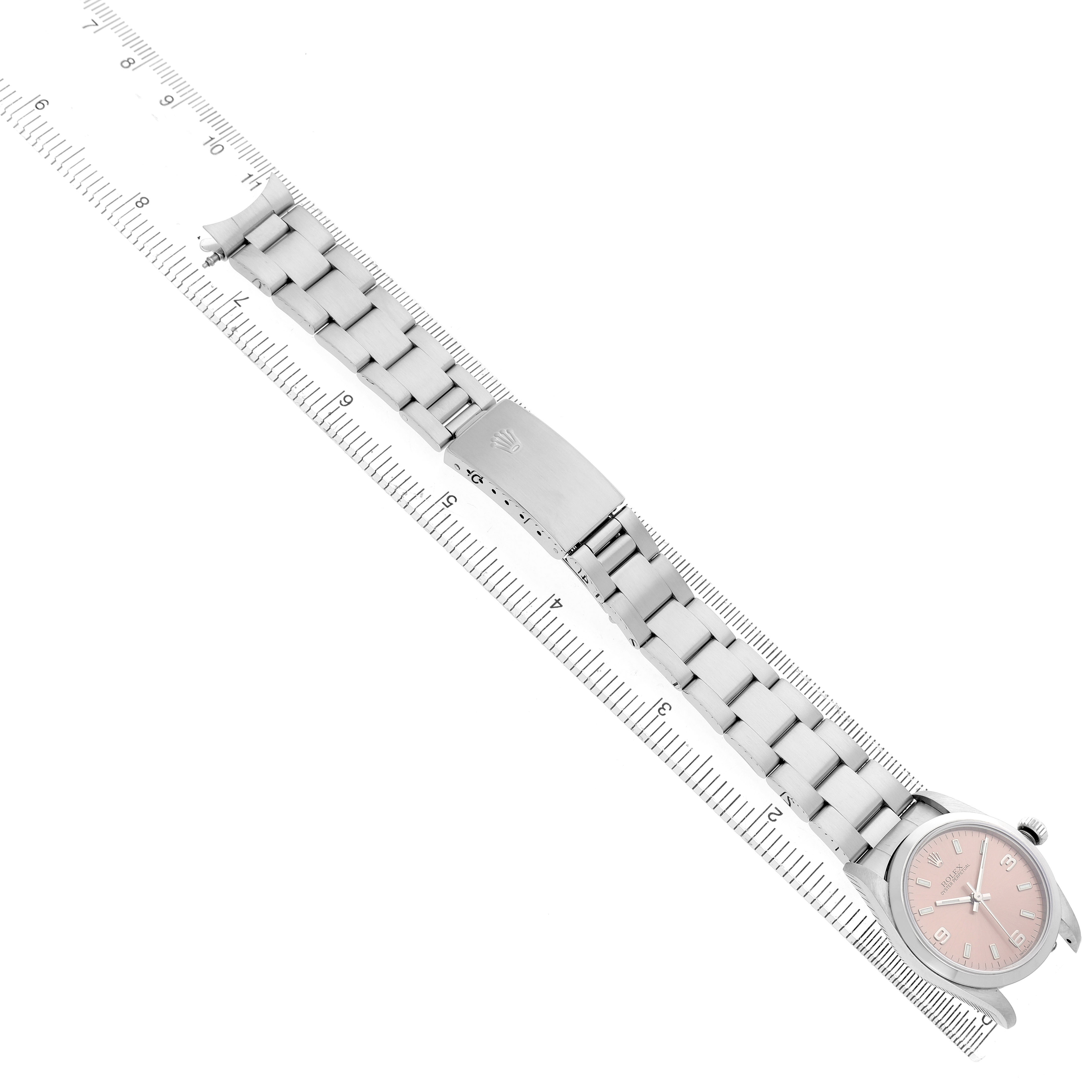 The Rolex Oyster Perpetual 77080 Women's Stainless Steel Pink Dial watch is shown from a top-down angle, highlighting the bracelet and clasp alongside a ruler for scale.