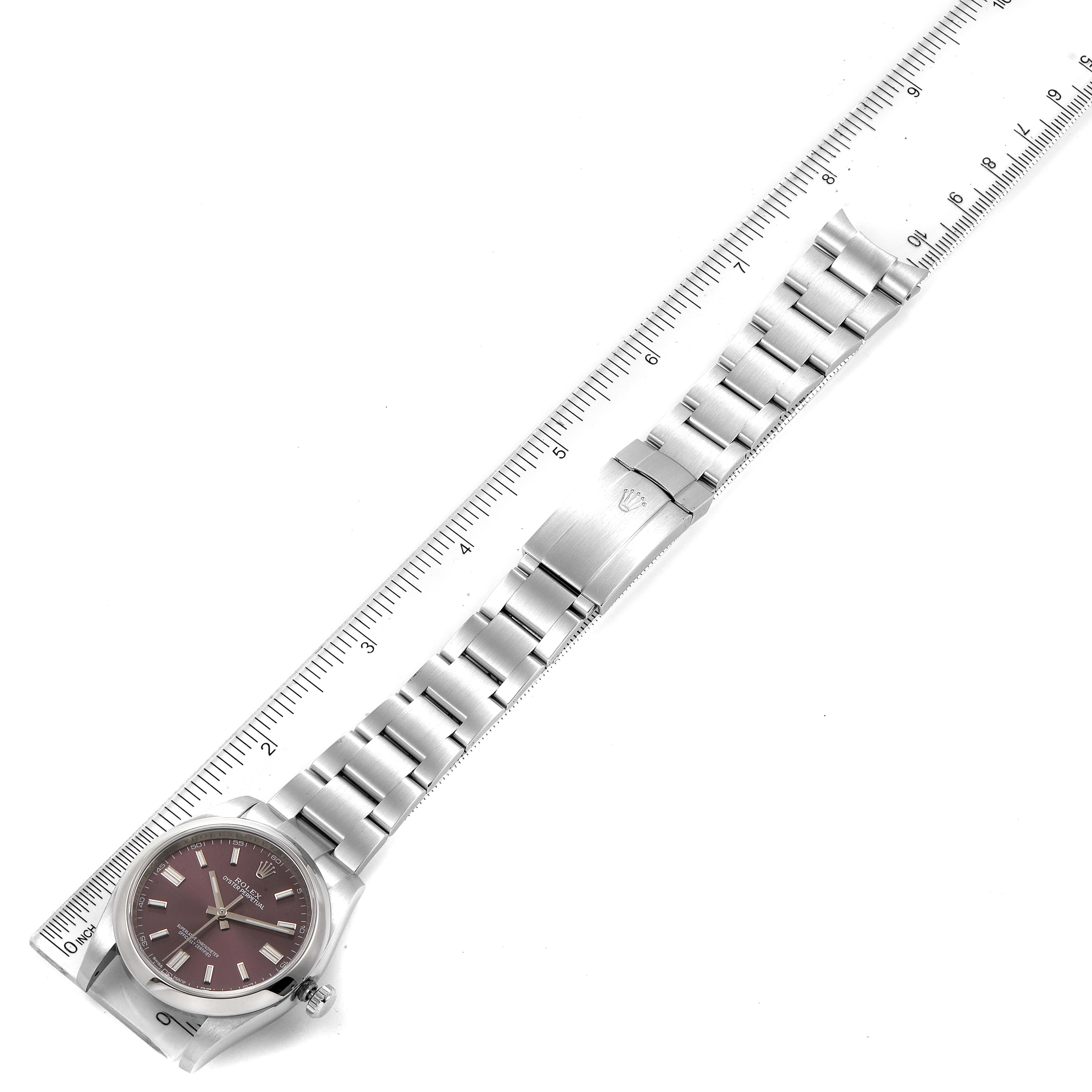 The image shows a top view of a Rolex Oyster Perpetual 116000 Men's Stainless Steel Burgundy Dial 116000 Men's Stainless Steel Burgundy Dial watch including its face, bracelet, and the clasp next to a ruler.
