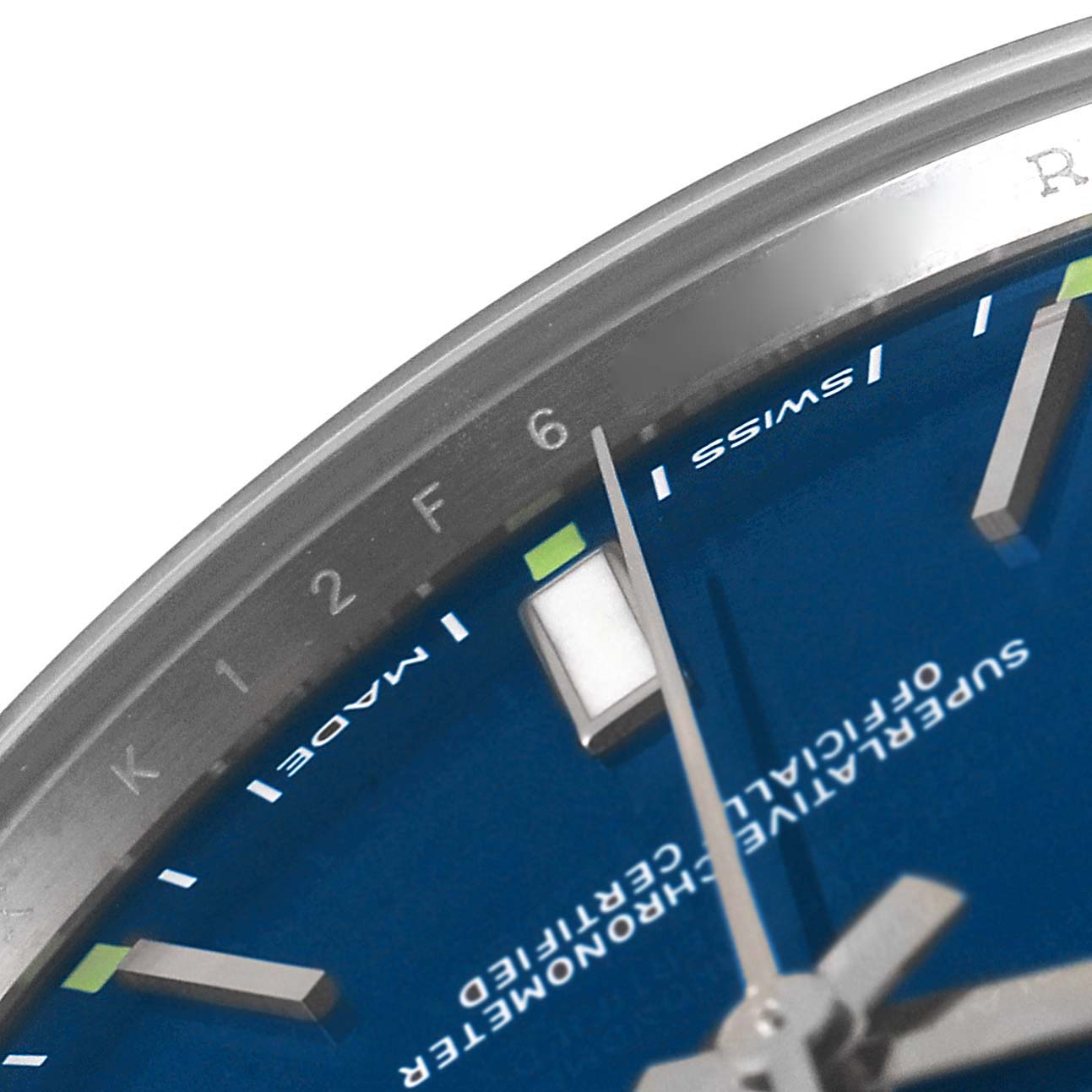 The image shows a close-up of the top left section of the dial of a Rolex Oyster Perpetual 114300 Men
s Stainless Steel Blue Dial 114300 Men
s Stainless Steel Blue Dial watch, focusing on the hour markers, minute track, and hands.