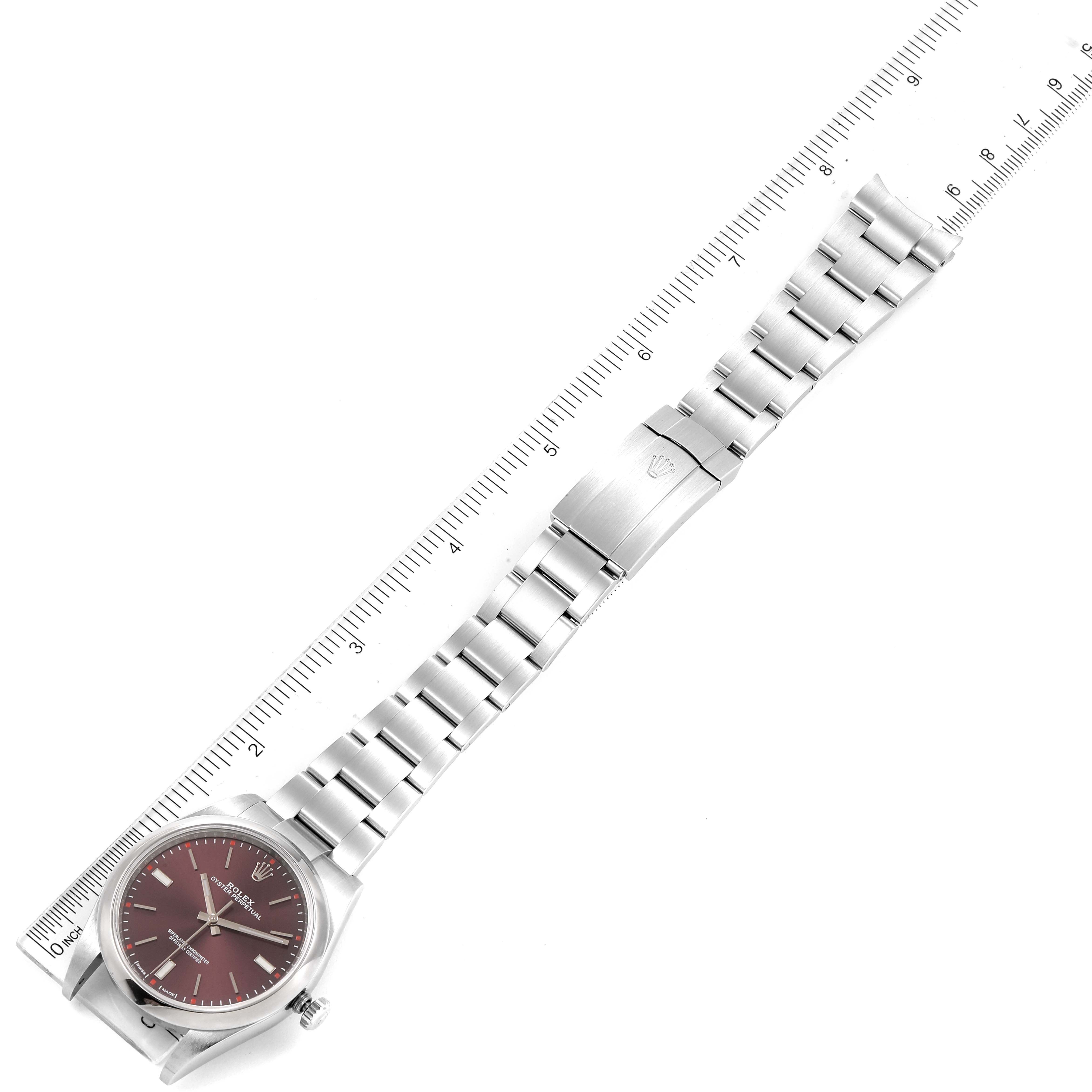 This image shows a Rolex Oyster Perpetual 114300 Men's Stainless Steel Burgundy Dial 114300 Men's Stainless Steel Burgundy Dial watch laid flat with its stainless steel strap, alongside a ruler for size reference.
