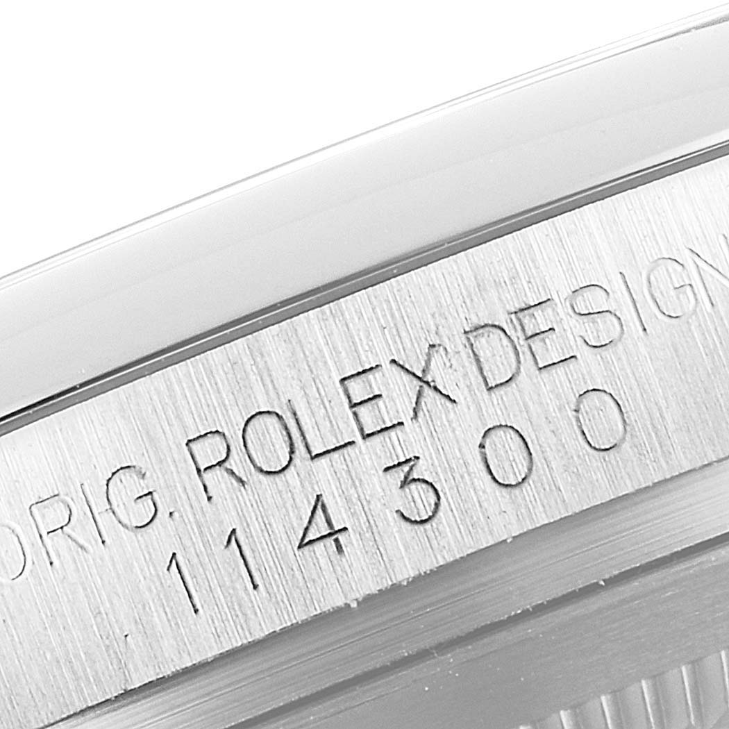 This image shows a close-up of the engraved case side on a Rolex Oyster Perpetual 114300 Men's Stainless Steel Burgundy Dial 114300 Men's Stainless Steel Burgundy Dial watch, displaying its design and model number.