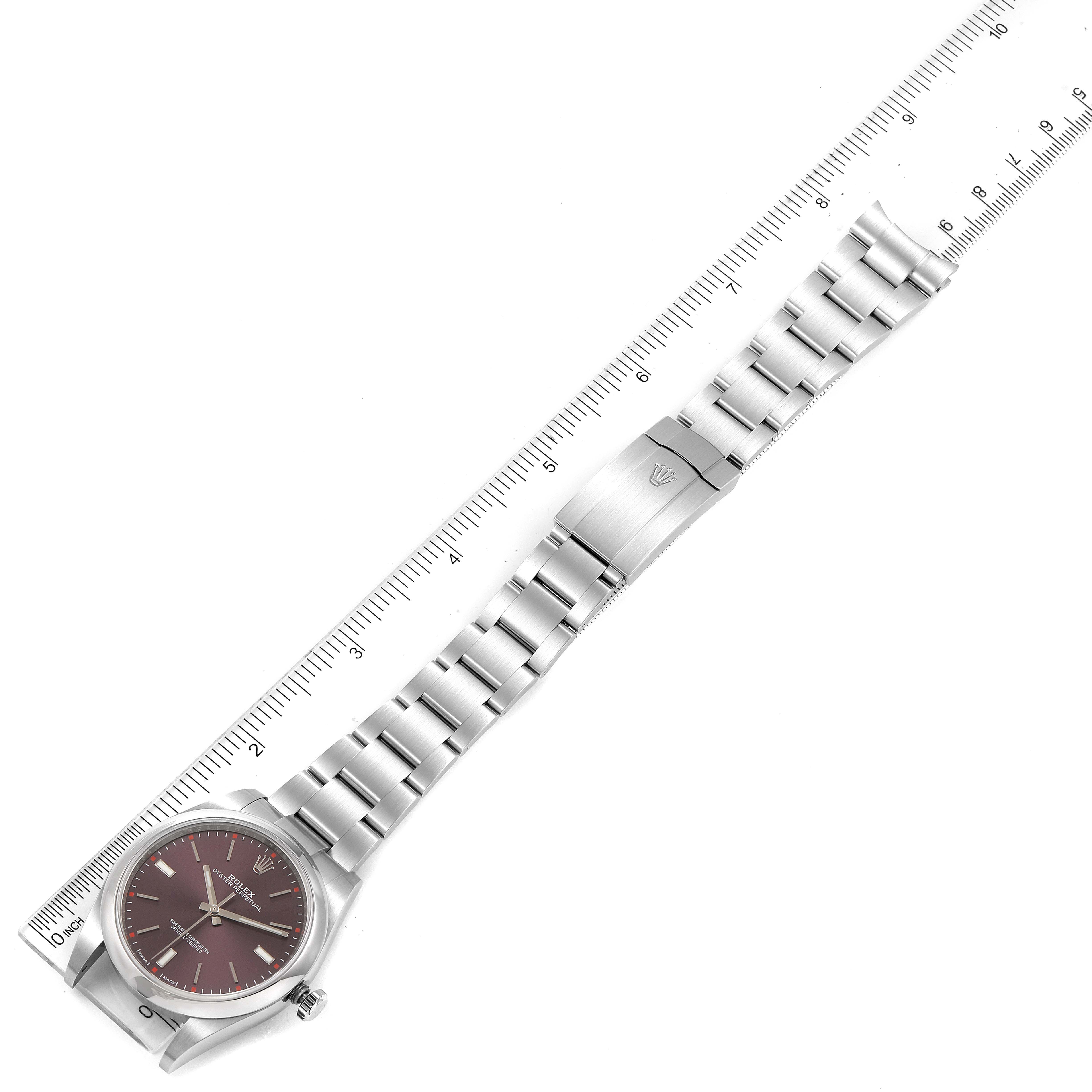 The Rolex Oyster Perpetual 114300 Men's Stainless Steel Burgundy Dial 114300 Men's Stainless Steel Burgundy Dial watch is shown from a top-down angle, displaying the face, bracelet, and clasp alongside a measurement ruler.