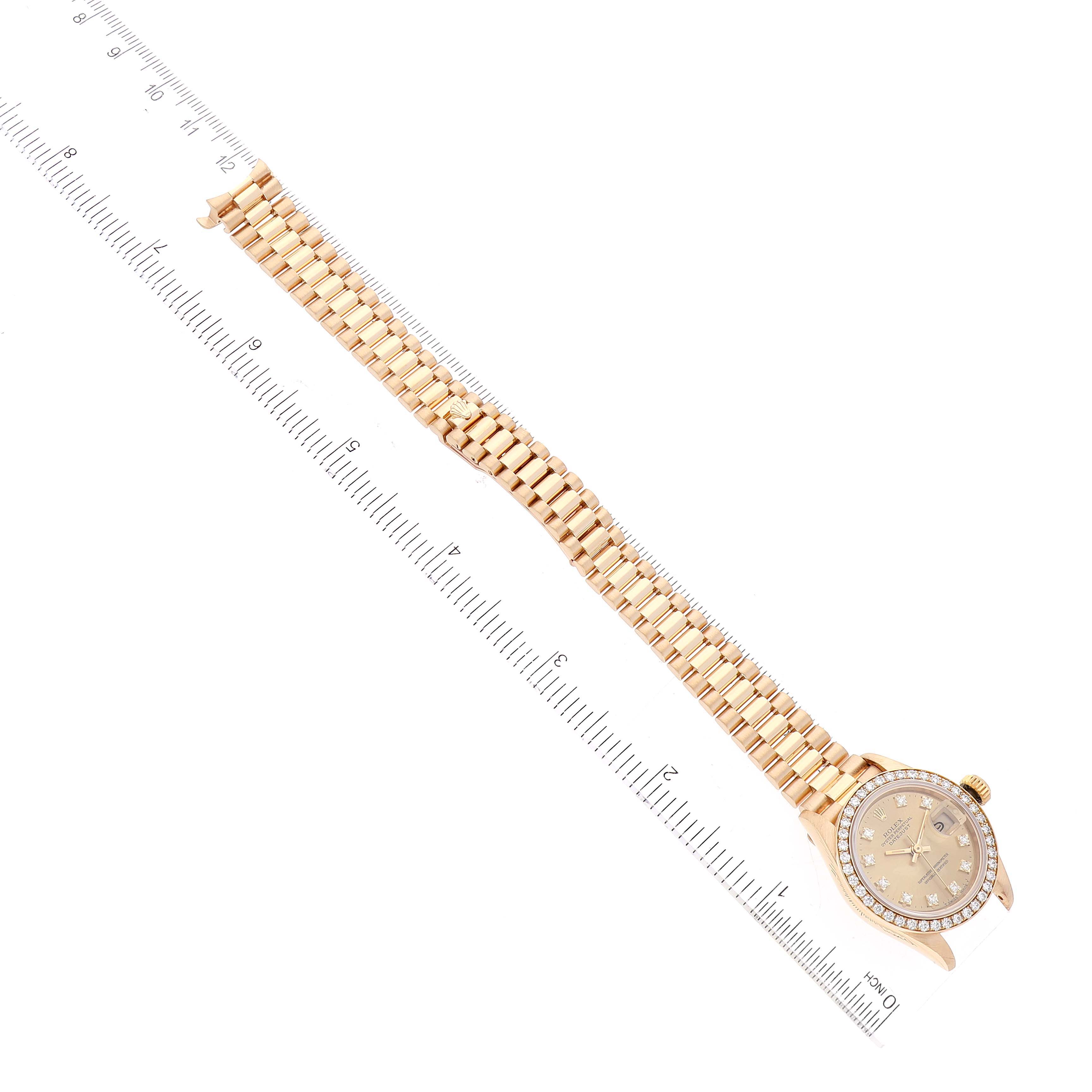The image shows a top-down view of a Rolex President 69138 Women
s Yellow Gold Champagne Dial 69138 Women
s Yellow Gold Champagne Dial model watch, displaying the face and full length of the band alongside a ruler.