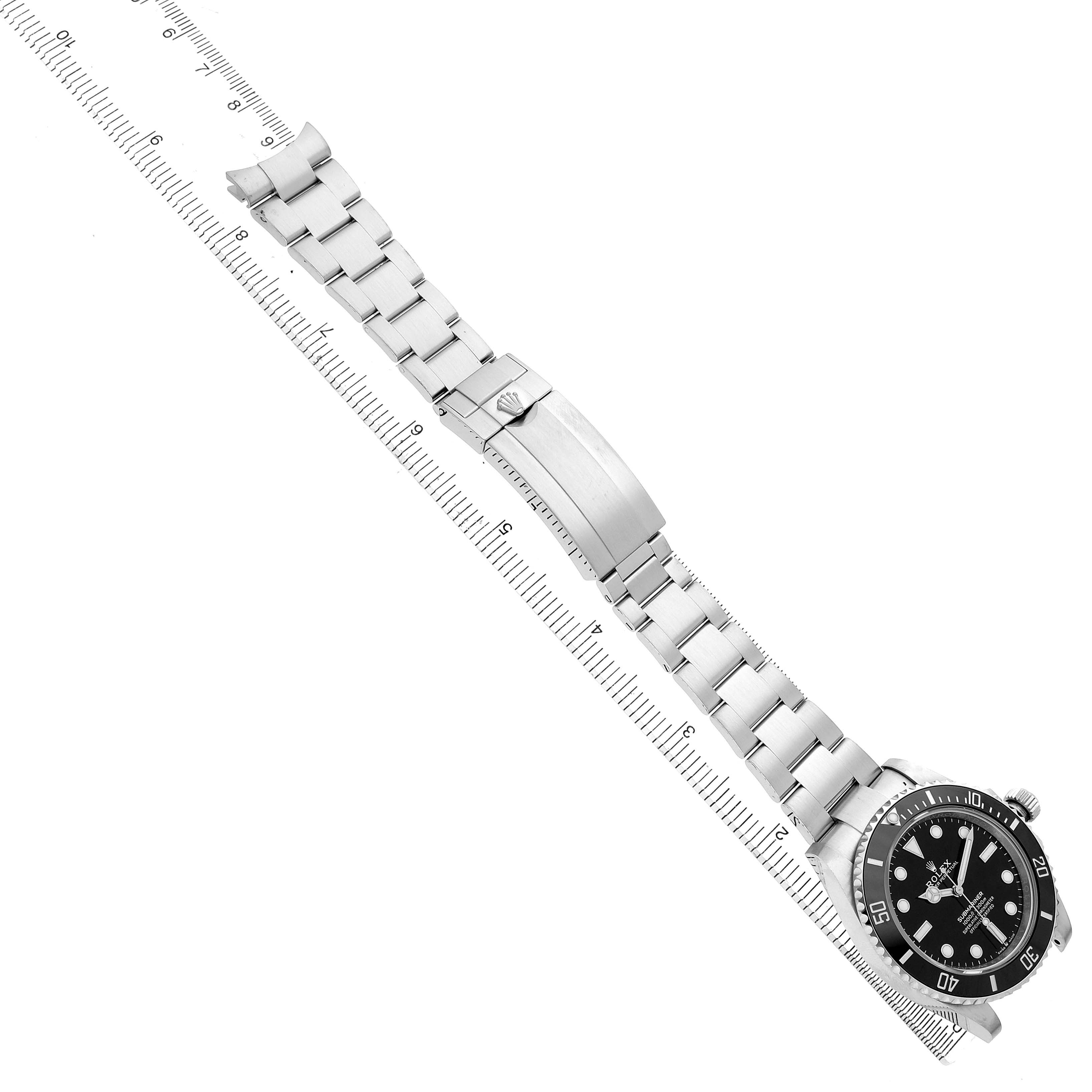 The image shows the Rolex Submariner M124060-0001 Men's Stainless Steel Black Dial watch from an overhead angle, displaying the bracelet and watch face alongside a ruler.