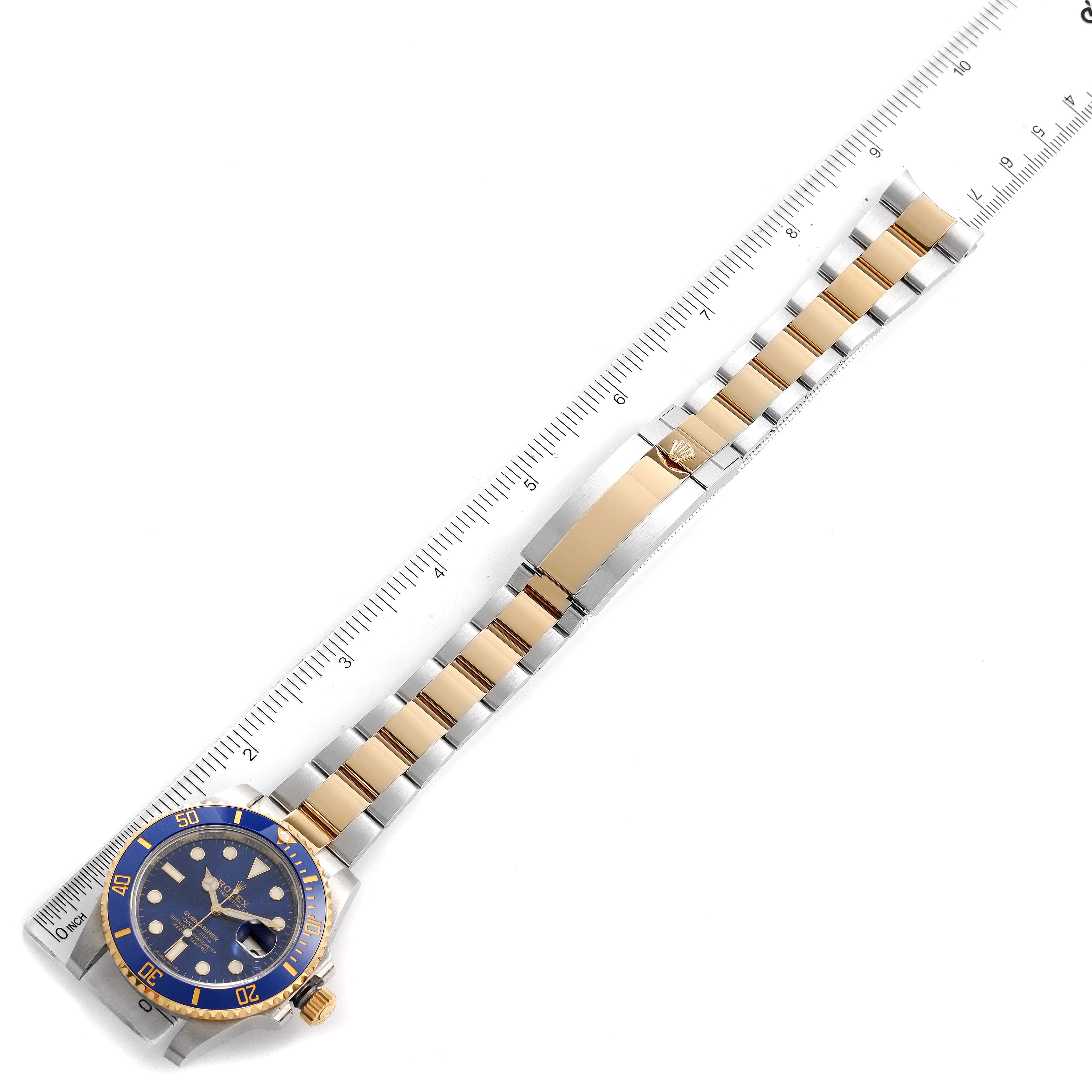 The Rolex Submariner 116613 Men
s Steel and Gold (two tone) Blue Dial 116613 Men
s Steel and Gold (two tone) Blue Dial watch is shown from a top-down angle, highlighting its full bracelet and face alongside a measuring ruler.