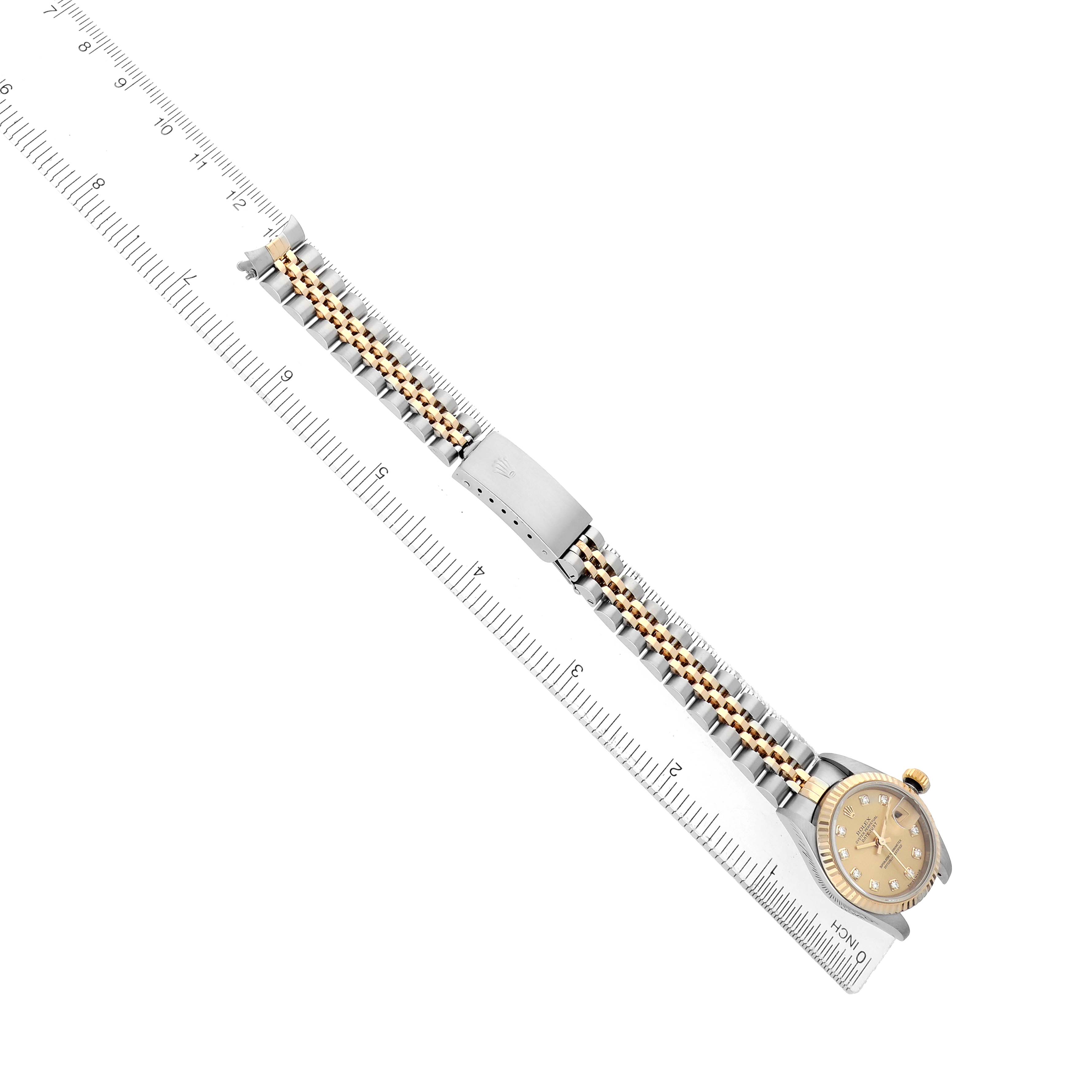 The Rolex Datejust 79173 Women
s Steel and Gold (two tone) Champagne Dial watch is displayed at a diagonal angle, showing the bracelet and clasp alongside a ruler for scale.