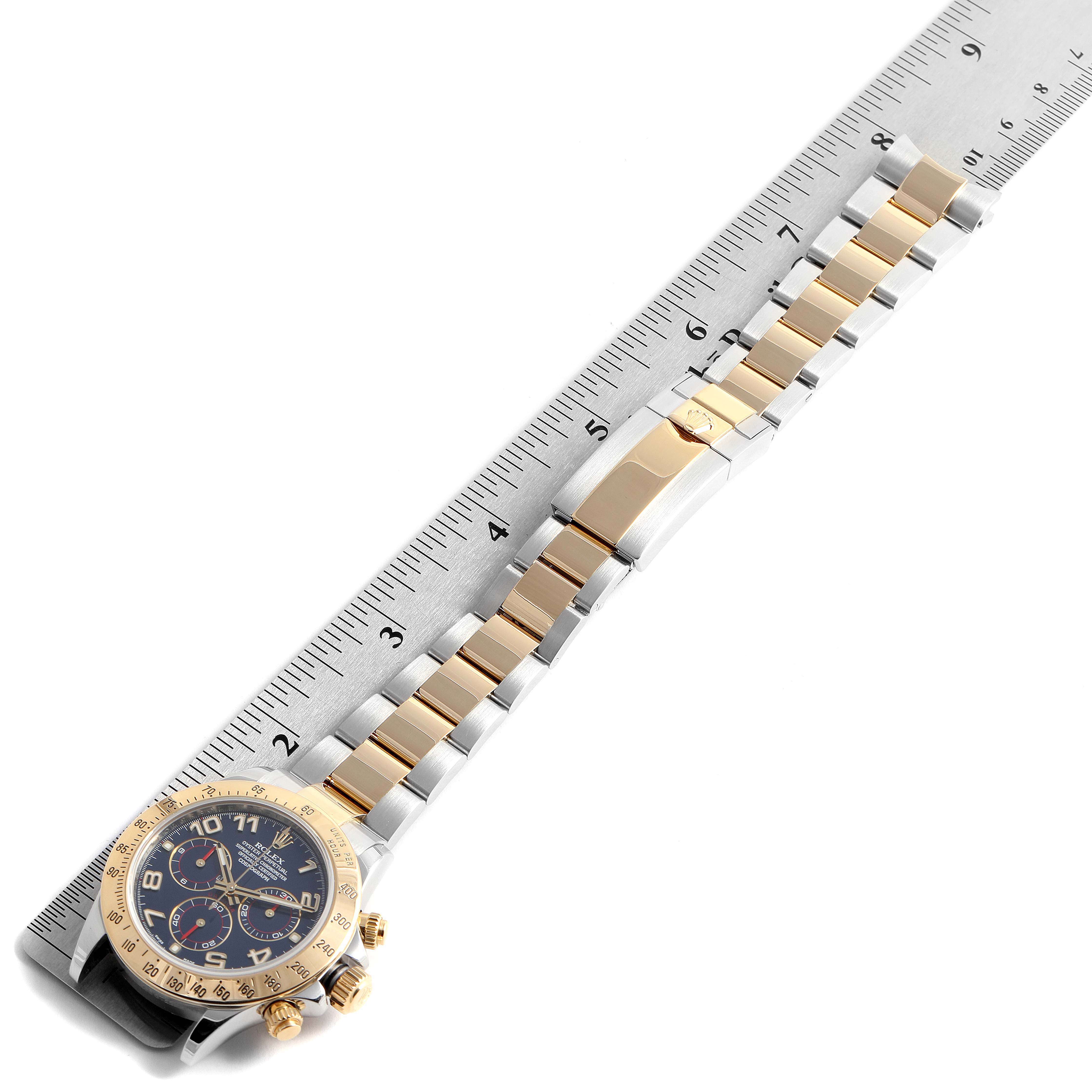 The image shows a Rolex Daytona 116523 Men's Steel and Gold (two tone) Blue Dial 116523 Men's Steel and Gold (two tone) Blue Dial watch laid flat with its band fully extended and a ruler for measurement.
