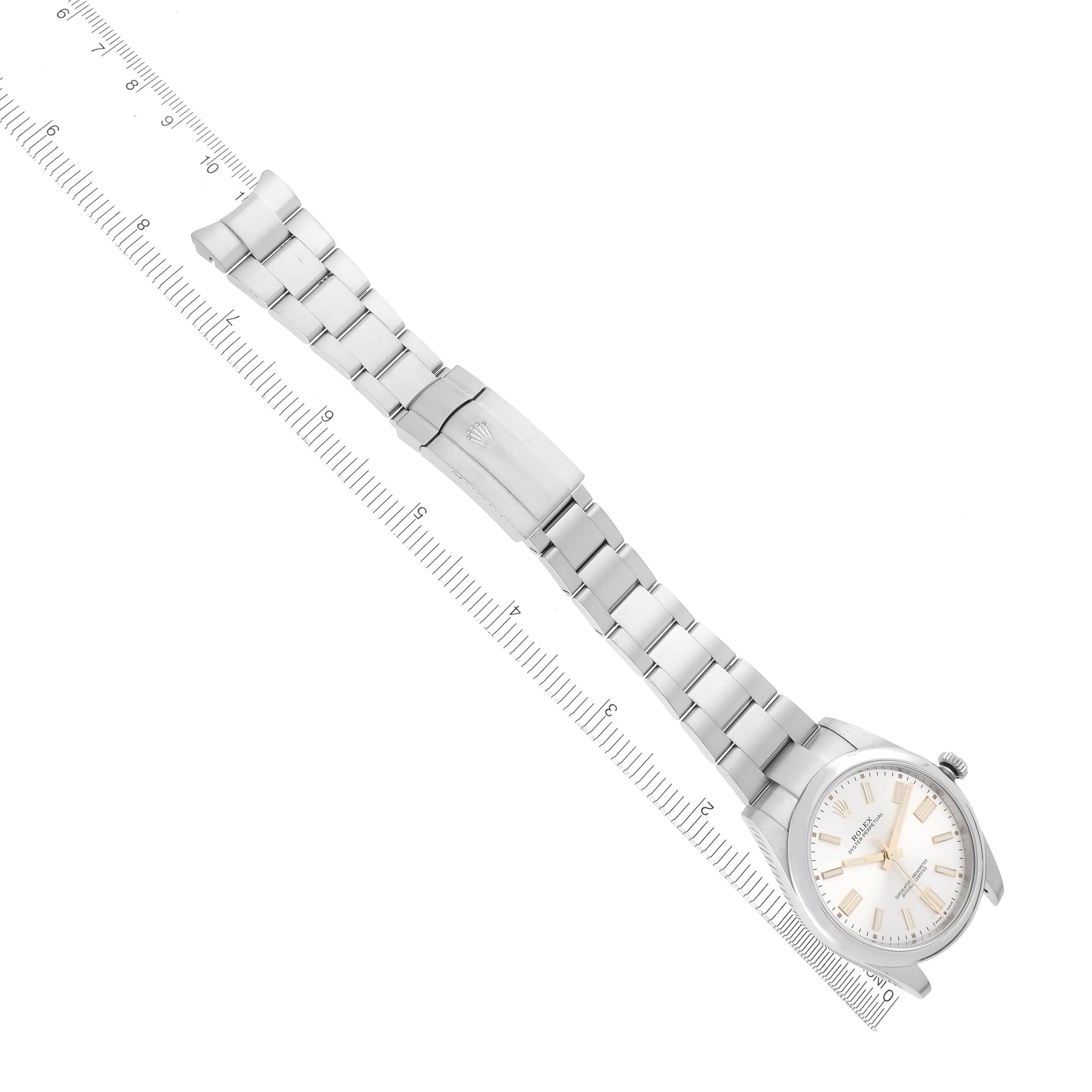 The Rolex Oyster Perpetual 124300 Men's Stainless Steel Silver Dial 124300 Men's Stainless Steel Silver Dial watch is displayed diagonally, showing the face, band, and deployment clasp against a measuring ruler.