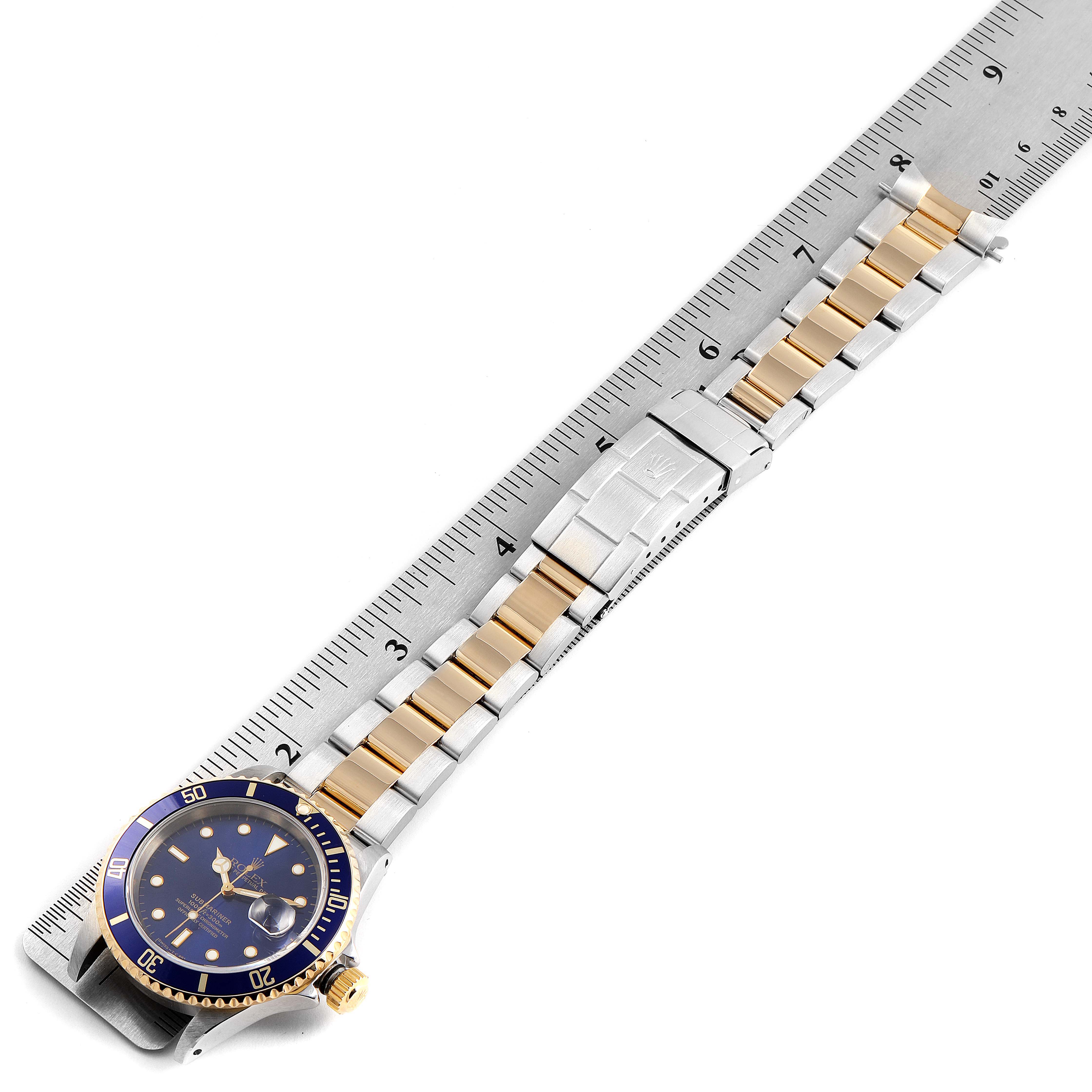 The Rolex Submariner 16613 Men's Steel and Gold (two tone) Blue Dial 16613 Men's Steel and Gold (two tone) Blue Dial watch is shown flat with a view of its dial, bezel, and two-tone bracelet next to a ruler.
