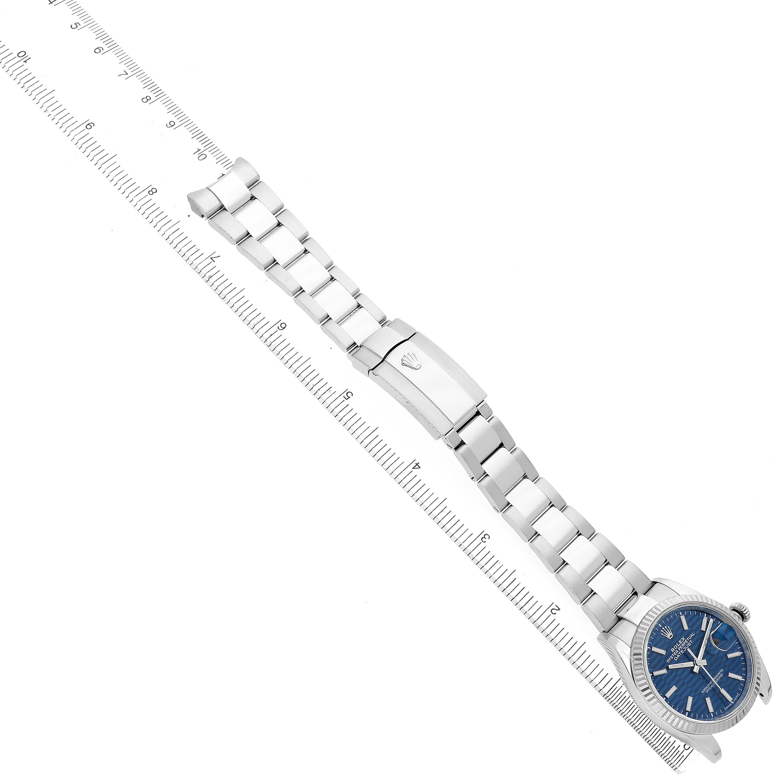 The Rolex Datejust 126234 Men's Stainless Steel Blue Dial watch is shown from a top-down angle, highlighting the bracelet, clasp, and blue dial next to a ruler for scale.