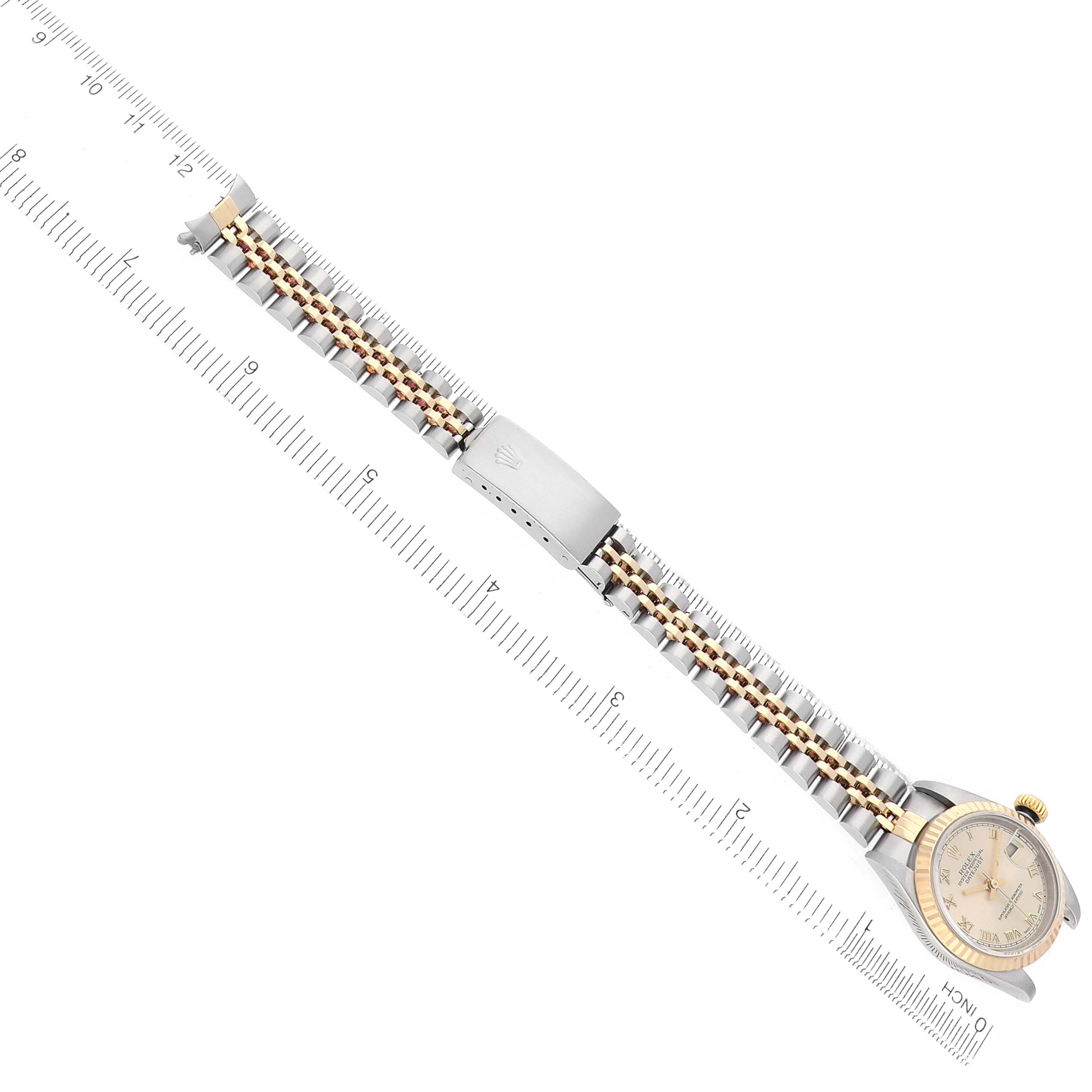The Rolex Datejust 79173 Women
s Steel and Gold (two tone) Champagne Dial watch is shown from a top-down view, highlighting the bracelet, clasp, case, and a visible partial dial on a ruler.