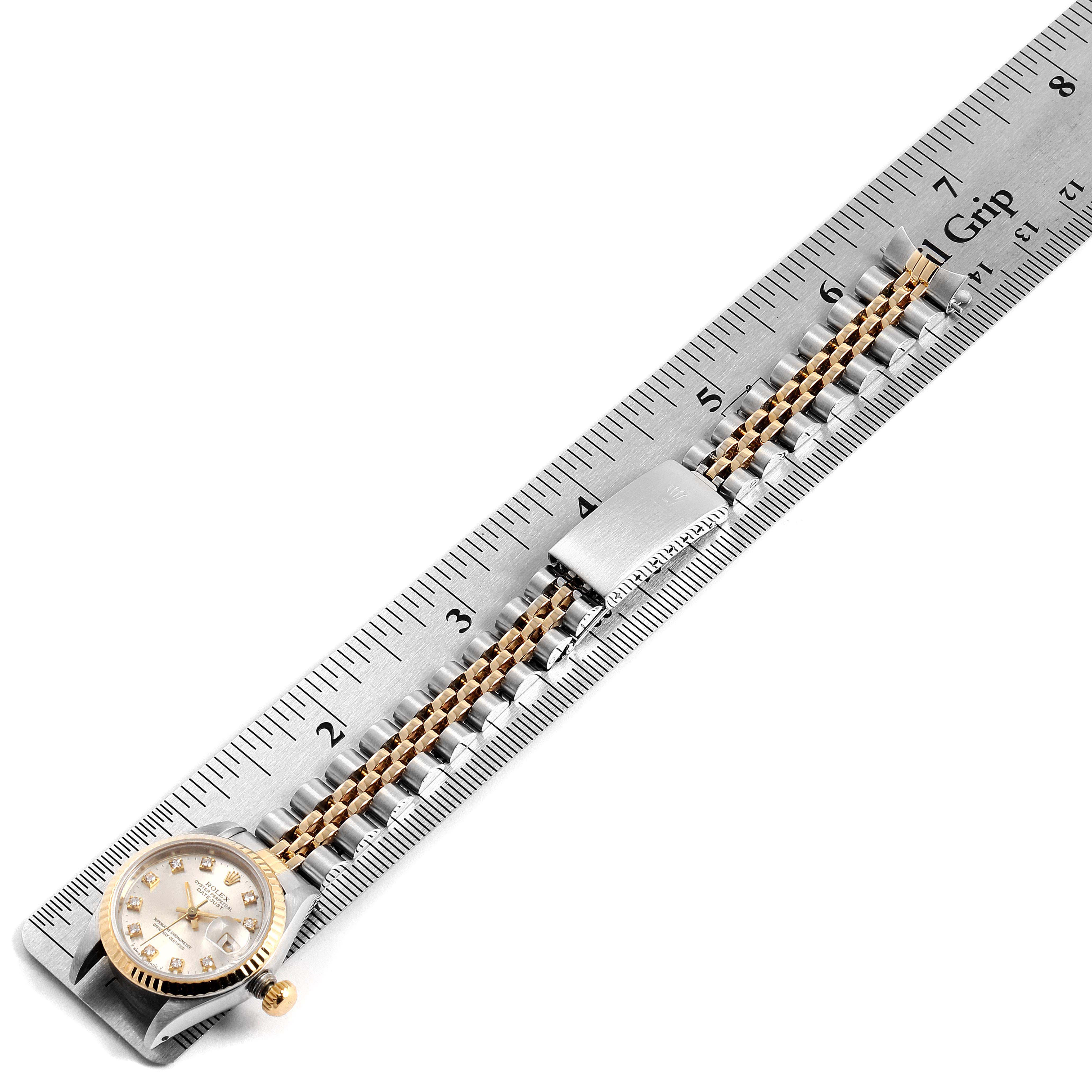 The Rolex Datejust 69173 Women
s Steel and Gold (two tone) Silver Dial 69173 Women
s Steel and Gold (two tone) Silver Dial watch is shown from a top-down angle with its face, bezel, and bracelet visible alongside a ruler.