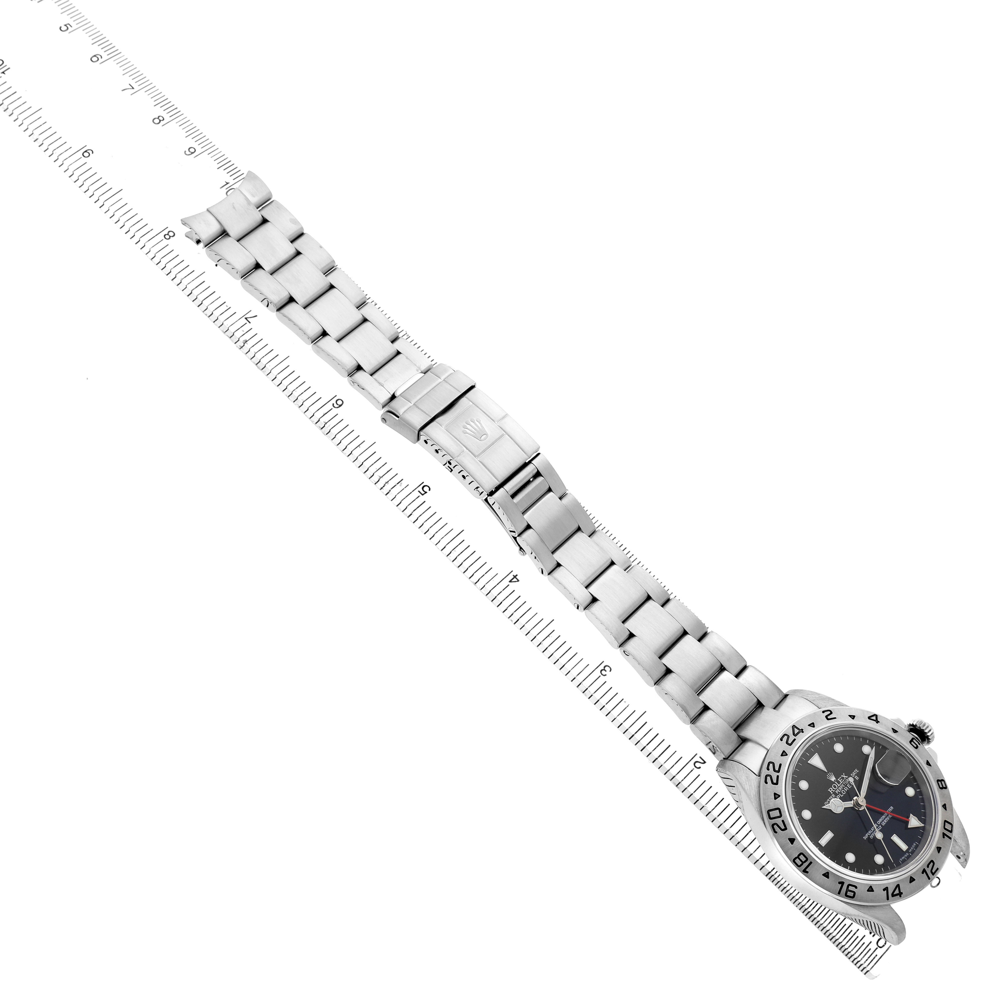 The Rolex Explorer 16570 Men's Stainless Steel Black Dial watch is shown from an overhead angle with a focus on the face, bracelet, and clasp next to a ruler for scale.
