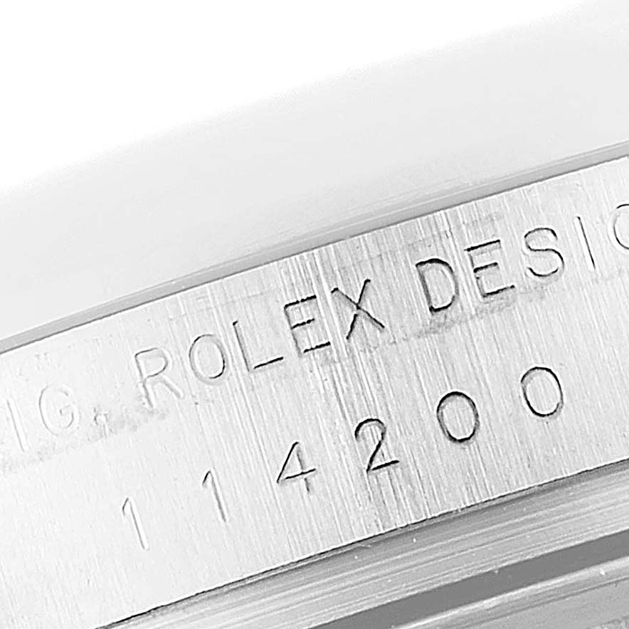 This image shows a close-up of the engraving on the case of a Rolex Oyster Perpetual 114200 Men's Stainless Steel Champagne Dial 114200 Men's Stainless Steel Champagne Dial watch.