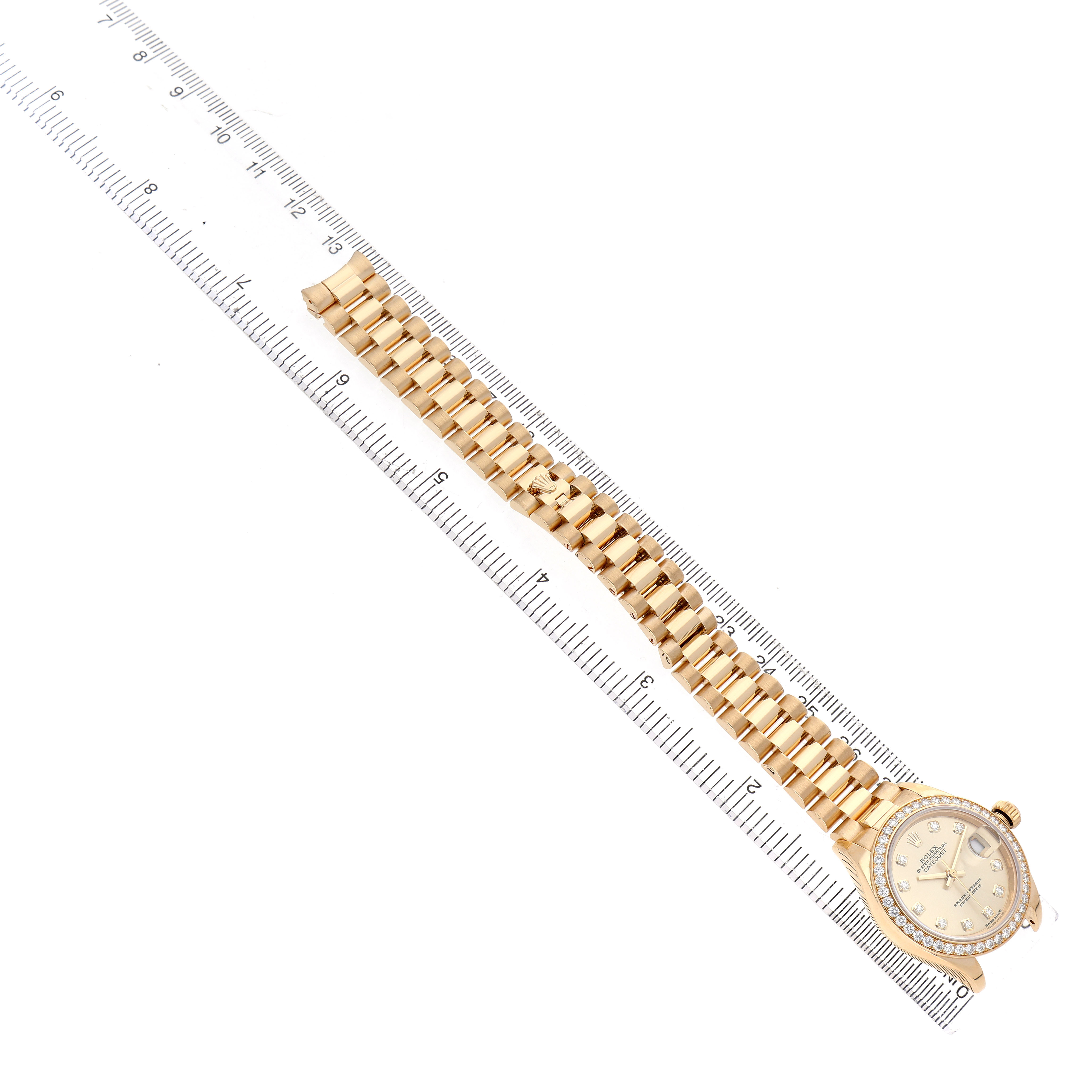 The Rolex President 279138 Women's Yellow Gold Champagne Dial watch is shown from a top-down angle, displaying its full bracelet and face alongside a ruler for scale.