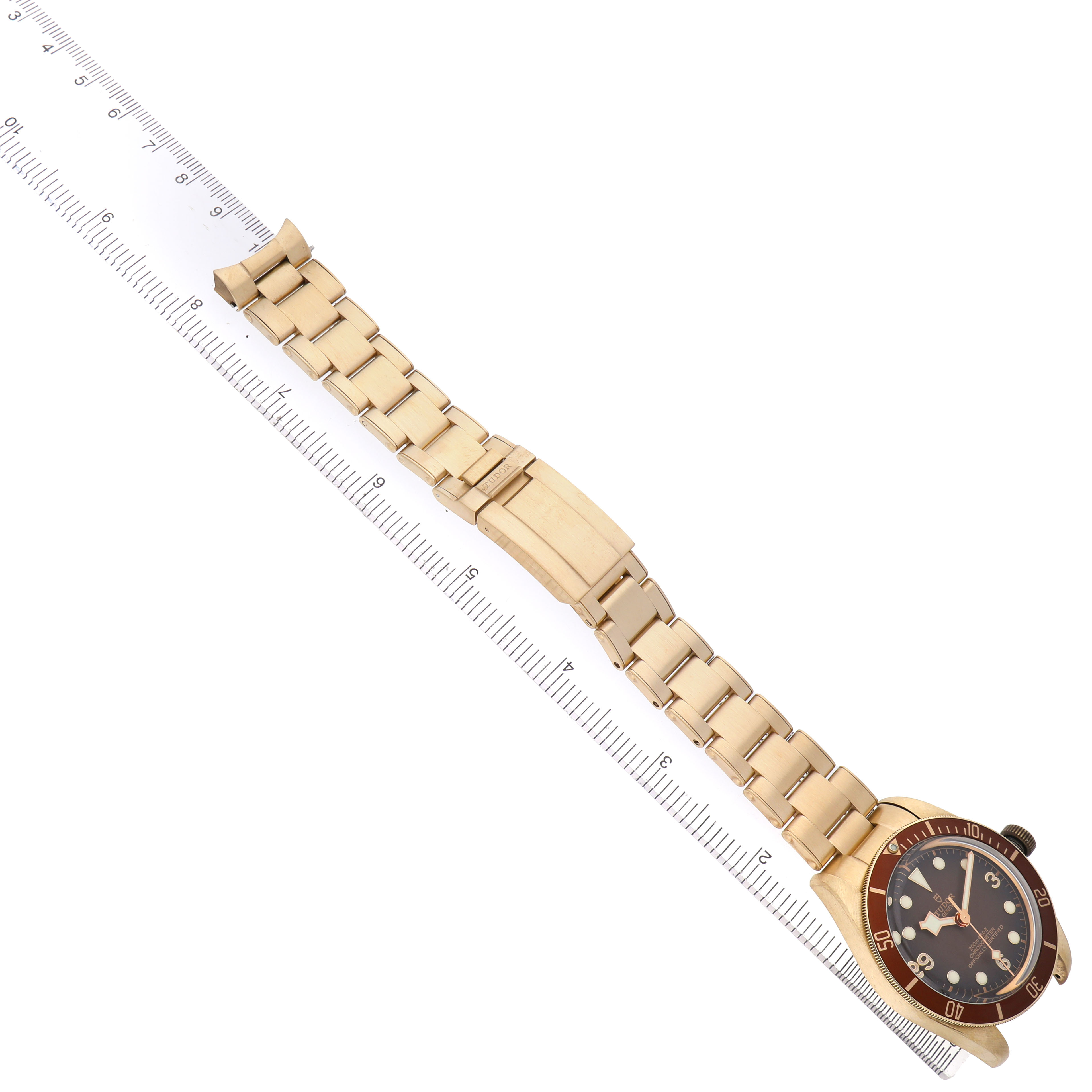 The Tudor Heritage Black Bay M79012M-0001 Men's Bronze Brown Dial watch is shown diagonally, highlighting the face, bezel, and full bracelet on a ruler.