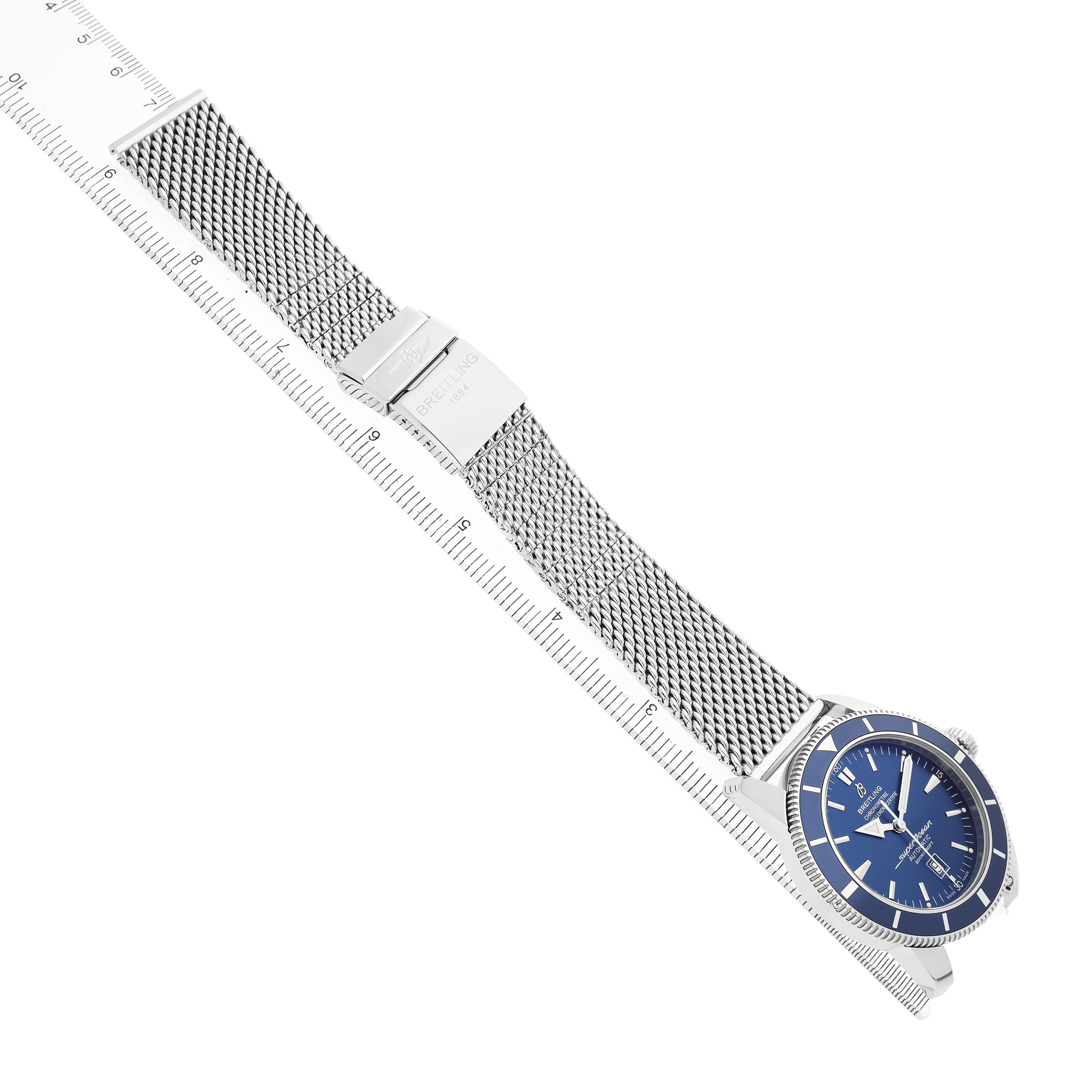 The Breitling Superocean A17320 Men's Stainless Steel Blue Dial watch is shown at an oblique angle, highlighting the blue face, mesh strap, and clasp, with a ruler for scale.