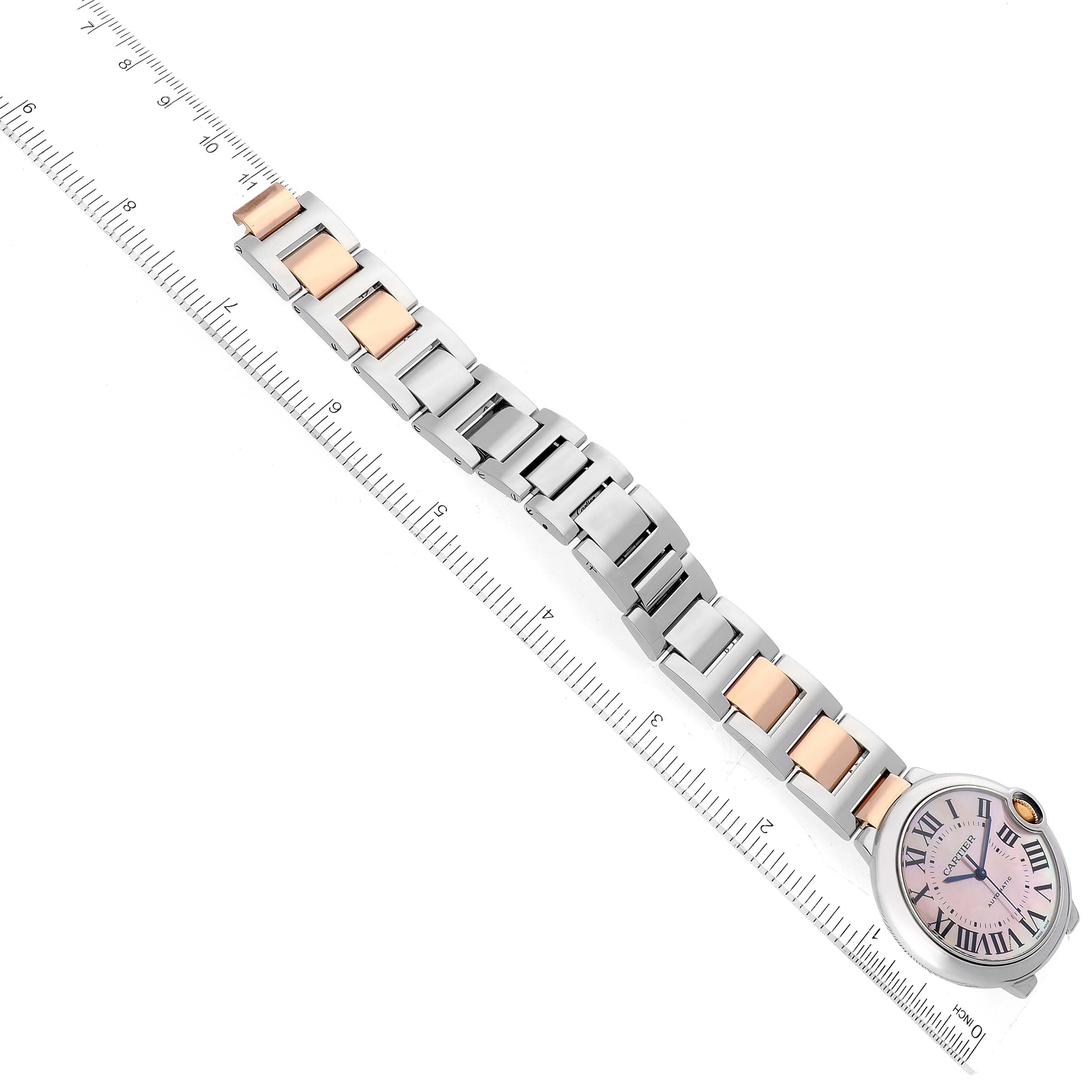 The image shows a Ballon Bleu model by Cartier from a top view, displaying the watch face and metal bracelet alongside a ruler for scale.