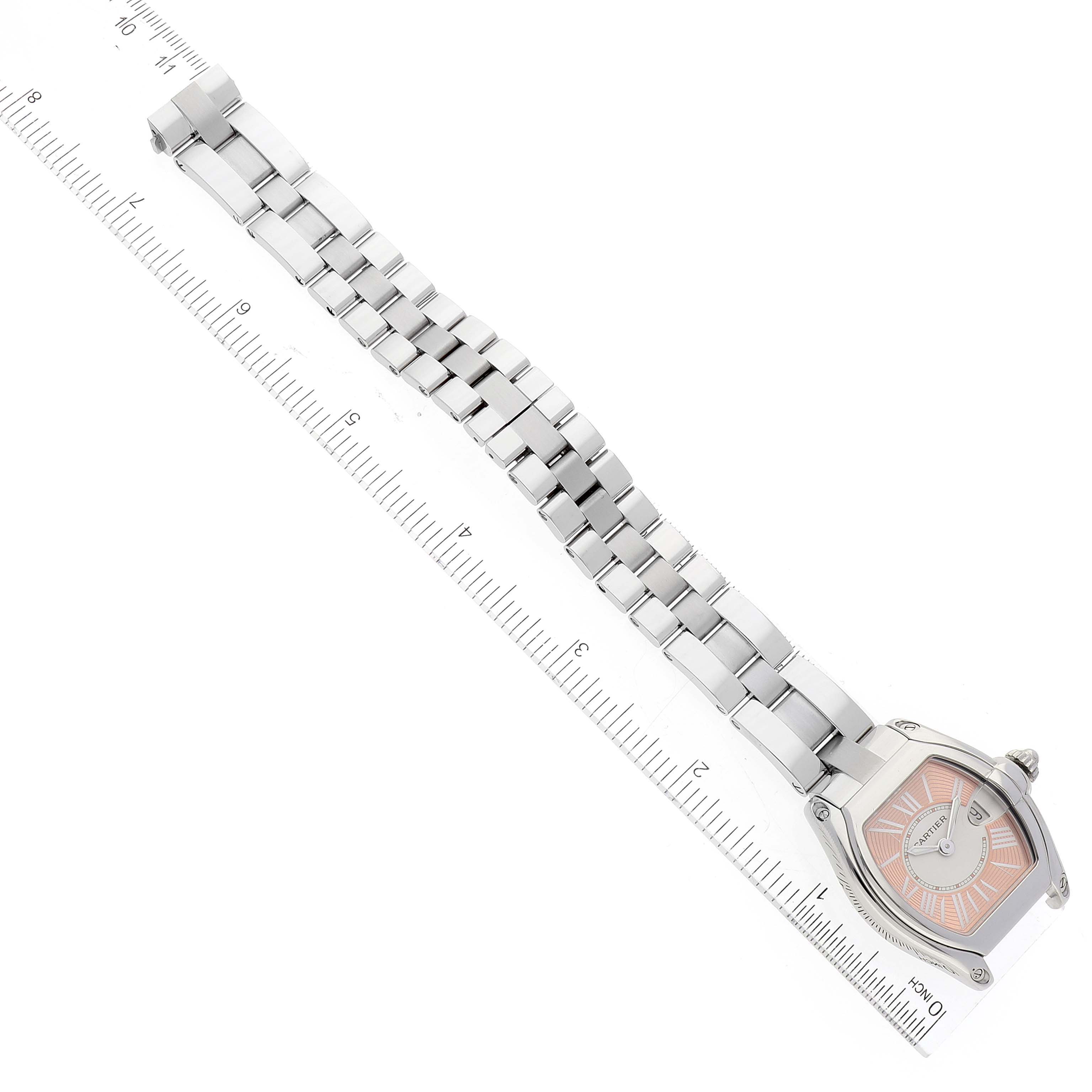 The image shows an overhead view of the Cartier Roadster W62054V3 Women's Stainless Steel Pink Dial W62054V3 Women's Stainless Steel Pink Dial watch, including the face and metal bracelet beside a measuring ruler.