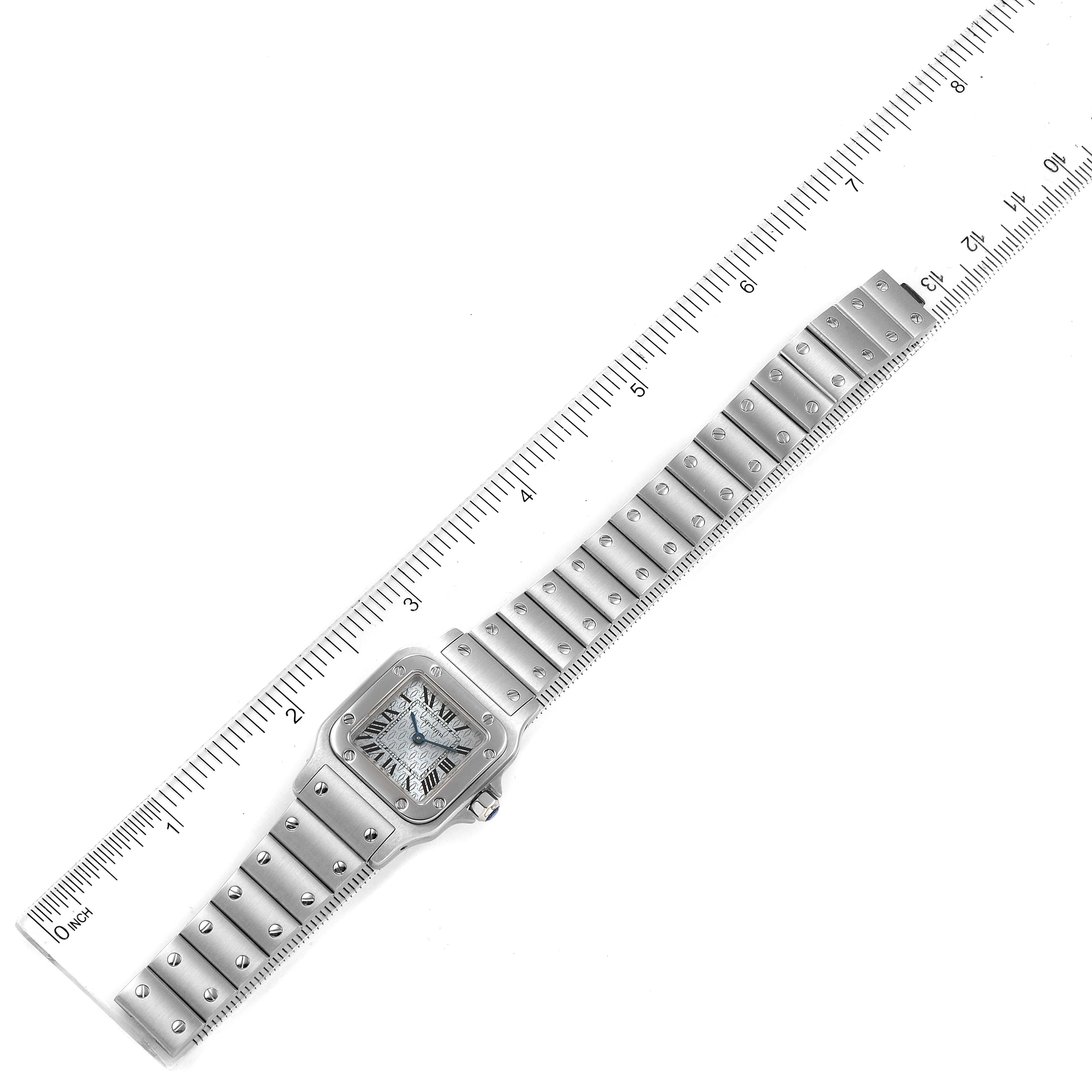 The Cartier Santos W20064D6 Women's Stainless Steel Blue Dial W20064D6 Women's Stainless Steel Blue Dial watch is shown flat, displaying its face, bezel, crown, and full metal bracelet alongside a ruler.