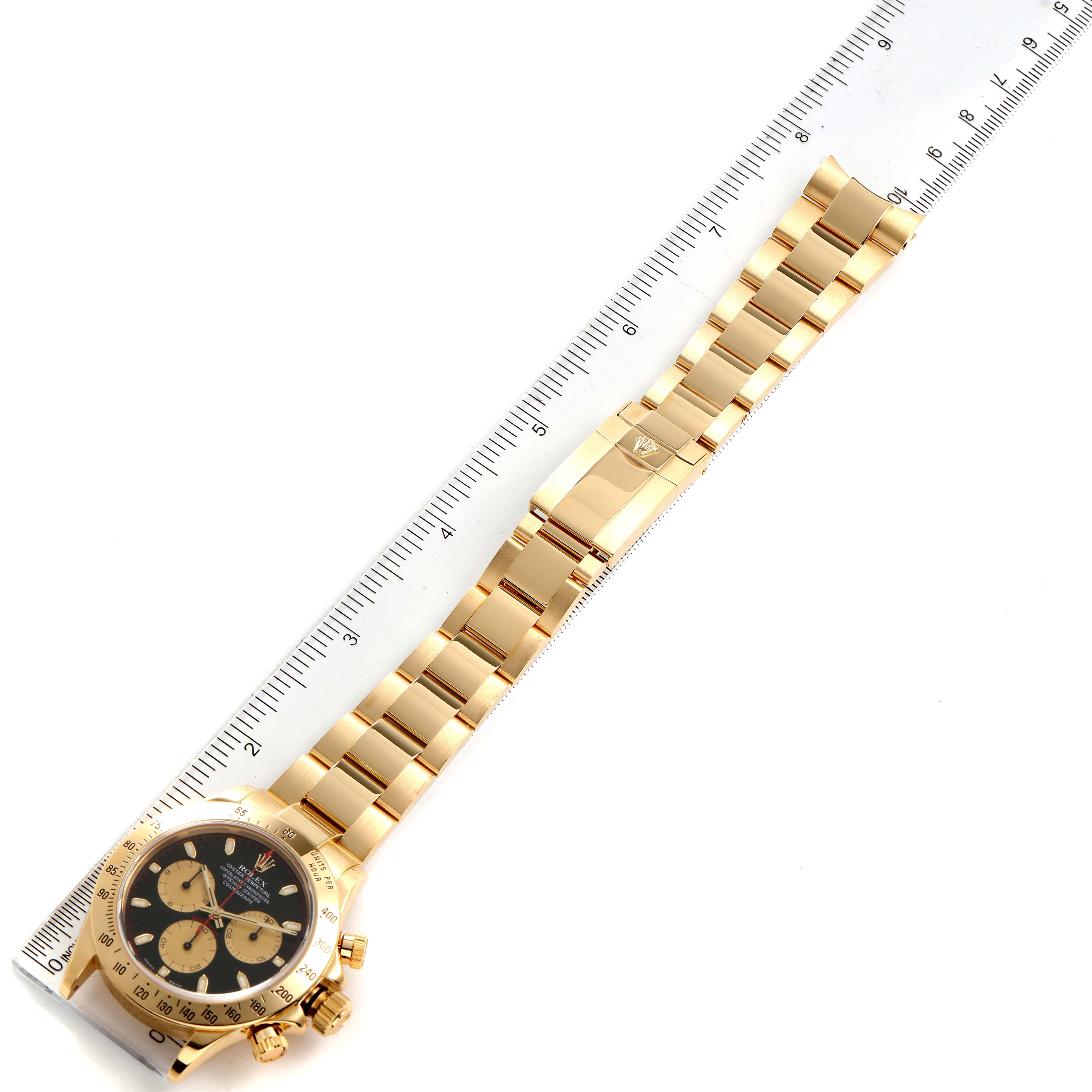 The image shows a Rolex Daytona 116528 Men's Yellow Gold Black Dial 116528 Men's Yellow Gold Black Dial watch laid flat next to a ruler, displaying the face, bracelet, and clasp.